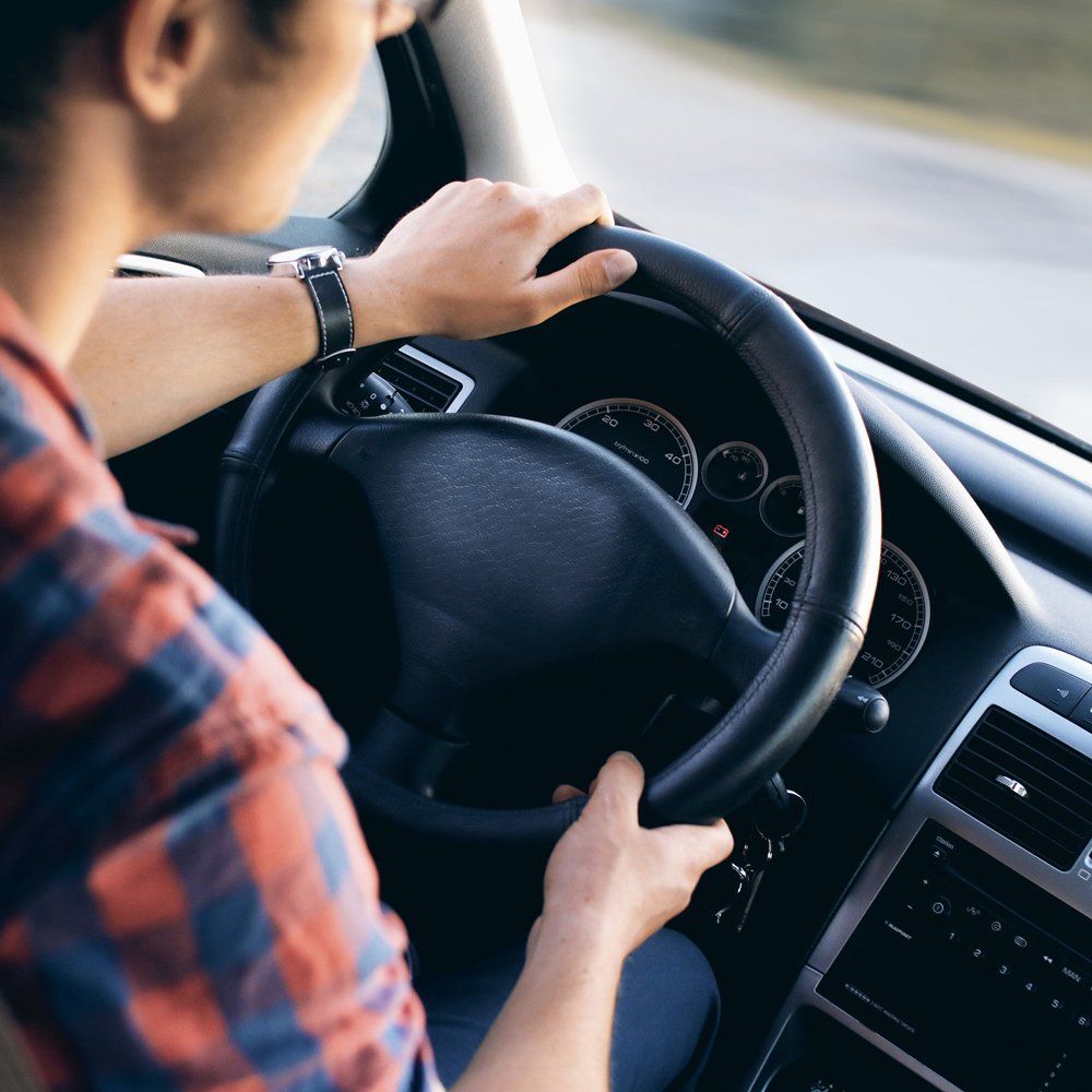 A man in a plaid shirt is driving a car