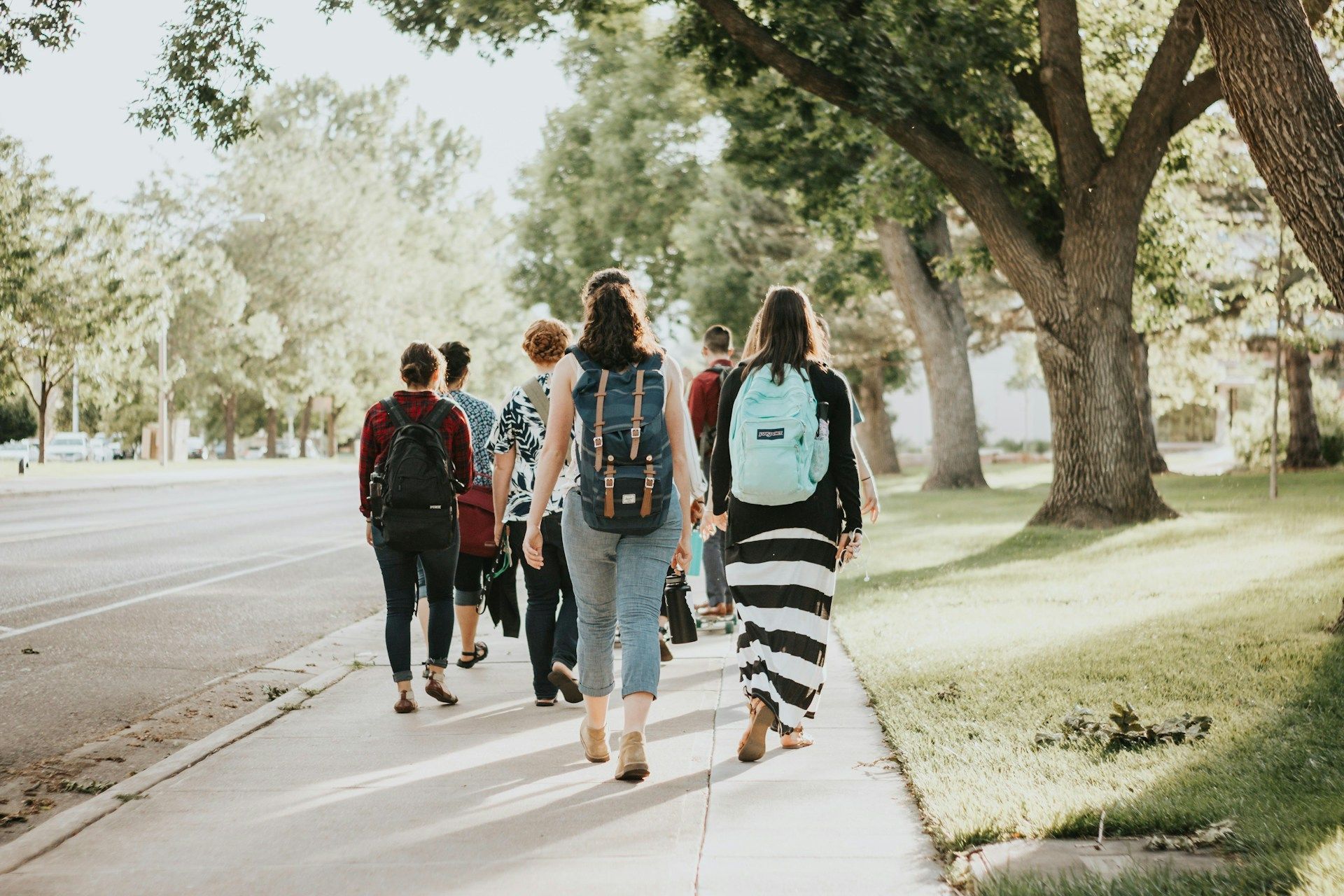 A group of people with backpacks are walking down a sidewalk.