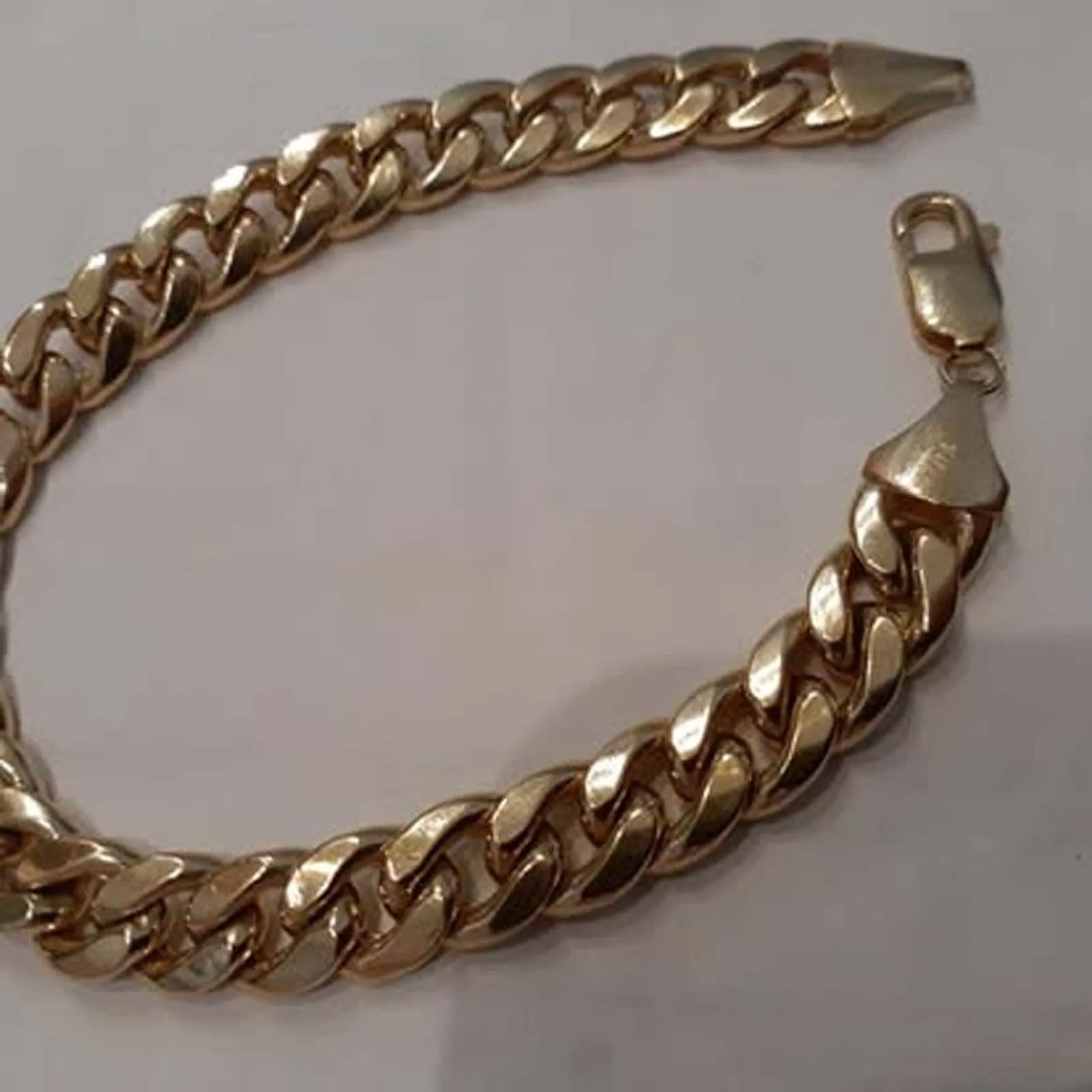 A close up of a gold chain bracelet on a white surface