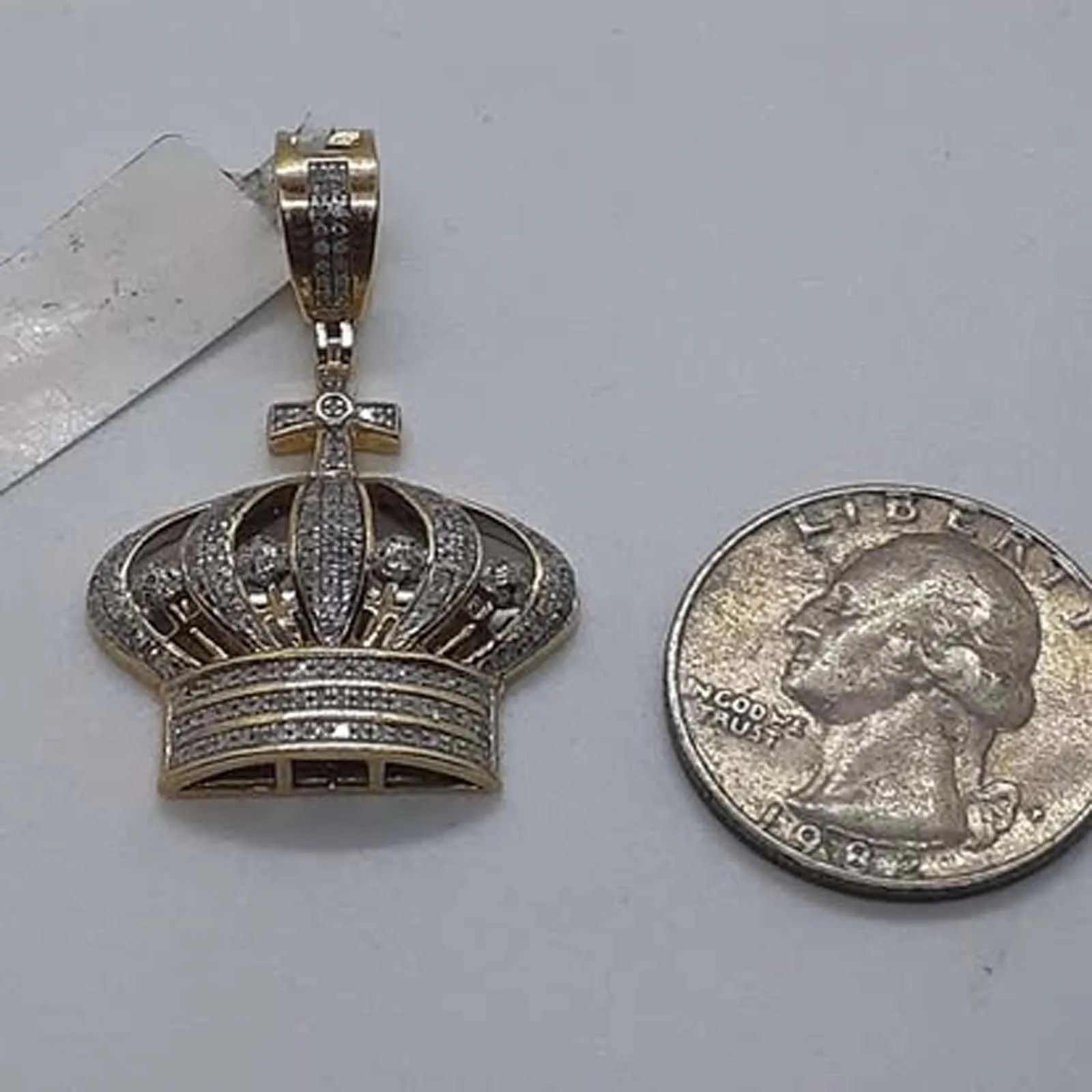A pendant in the shape of a crown is next to a quarter.