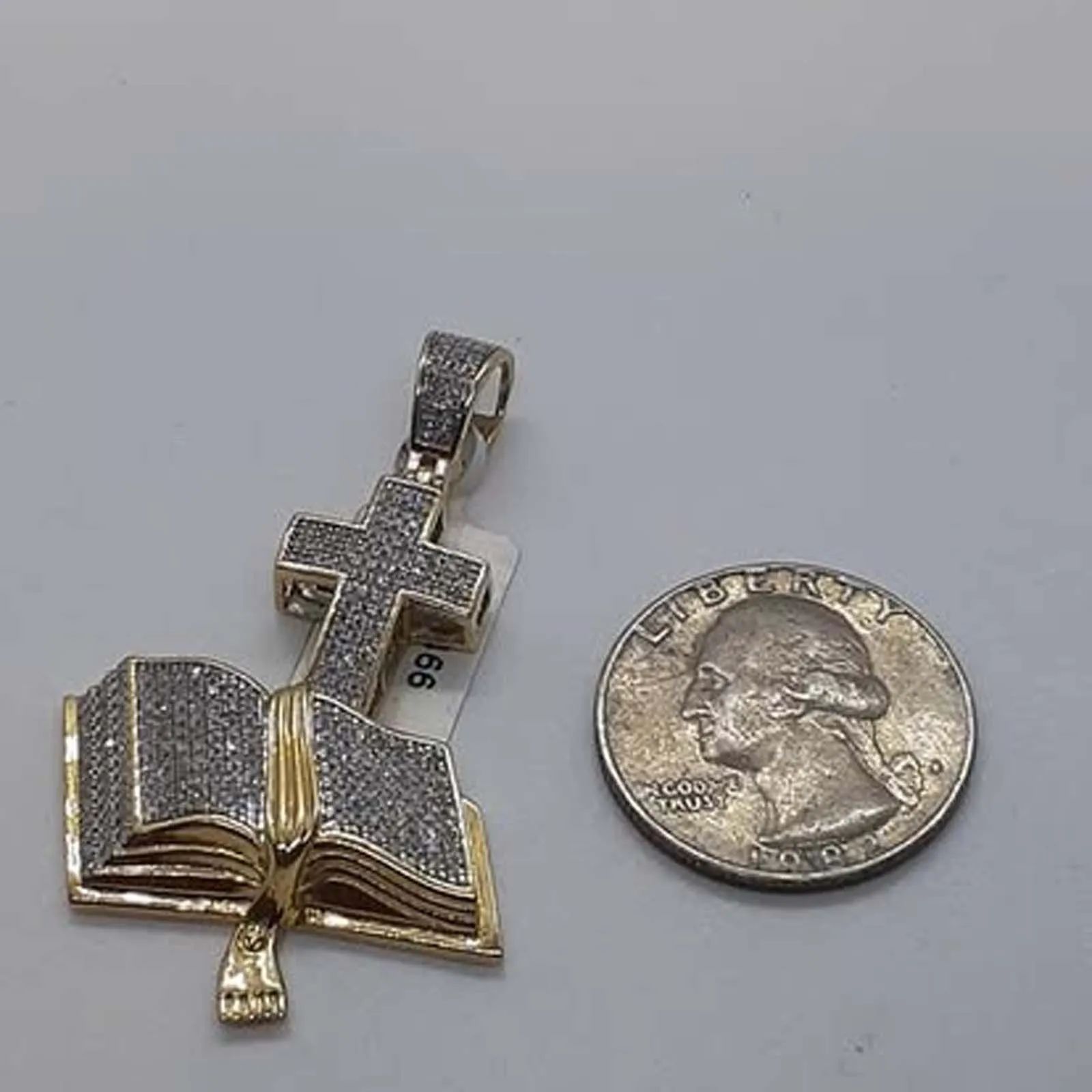 A pendant in the shape of an open book next to a quarter