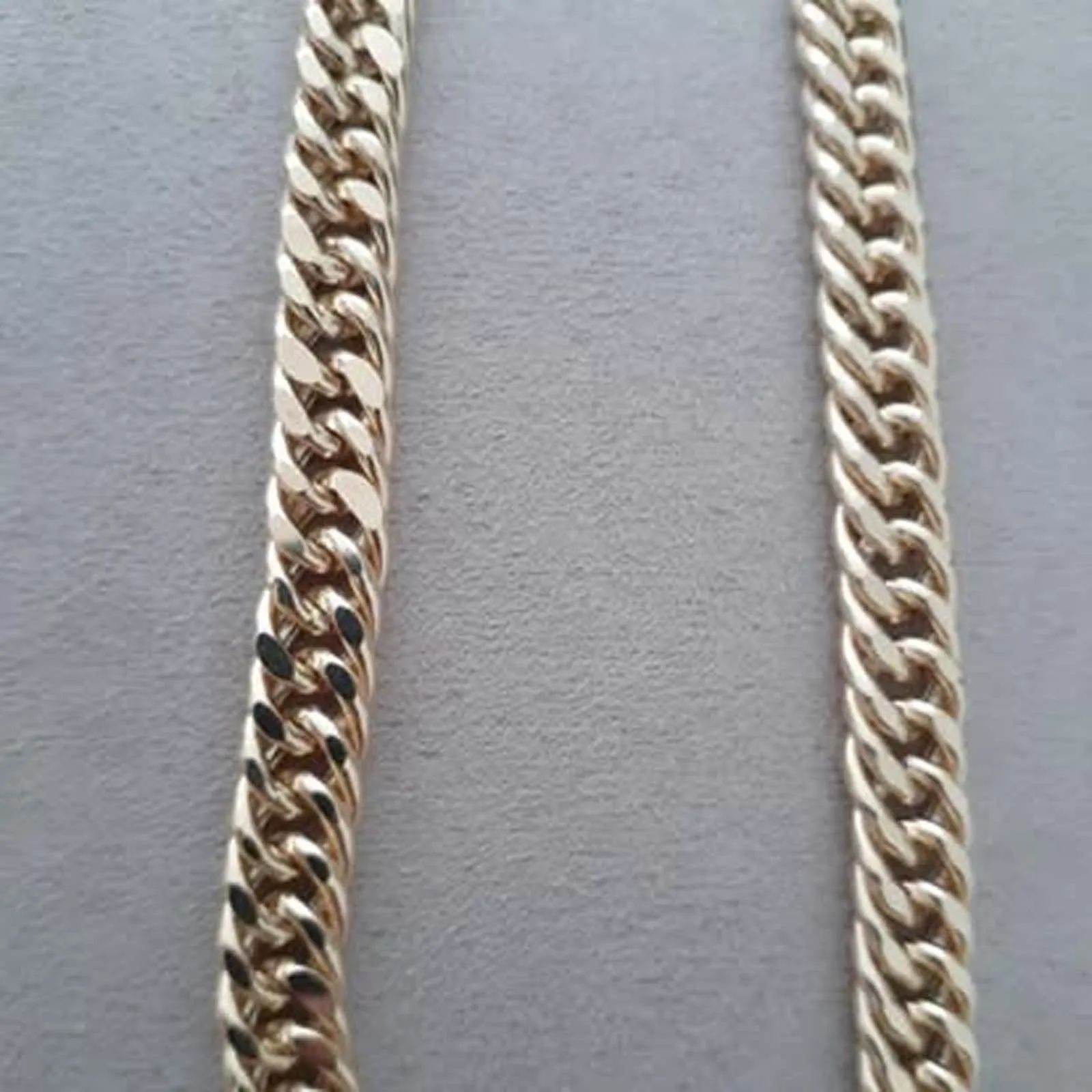 A close up of a gold chain on a white surface.