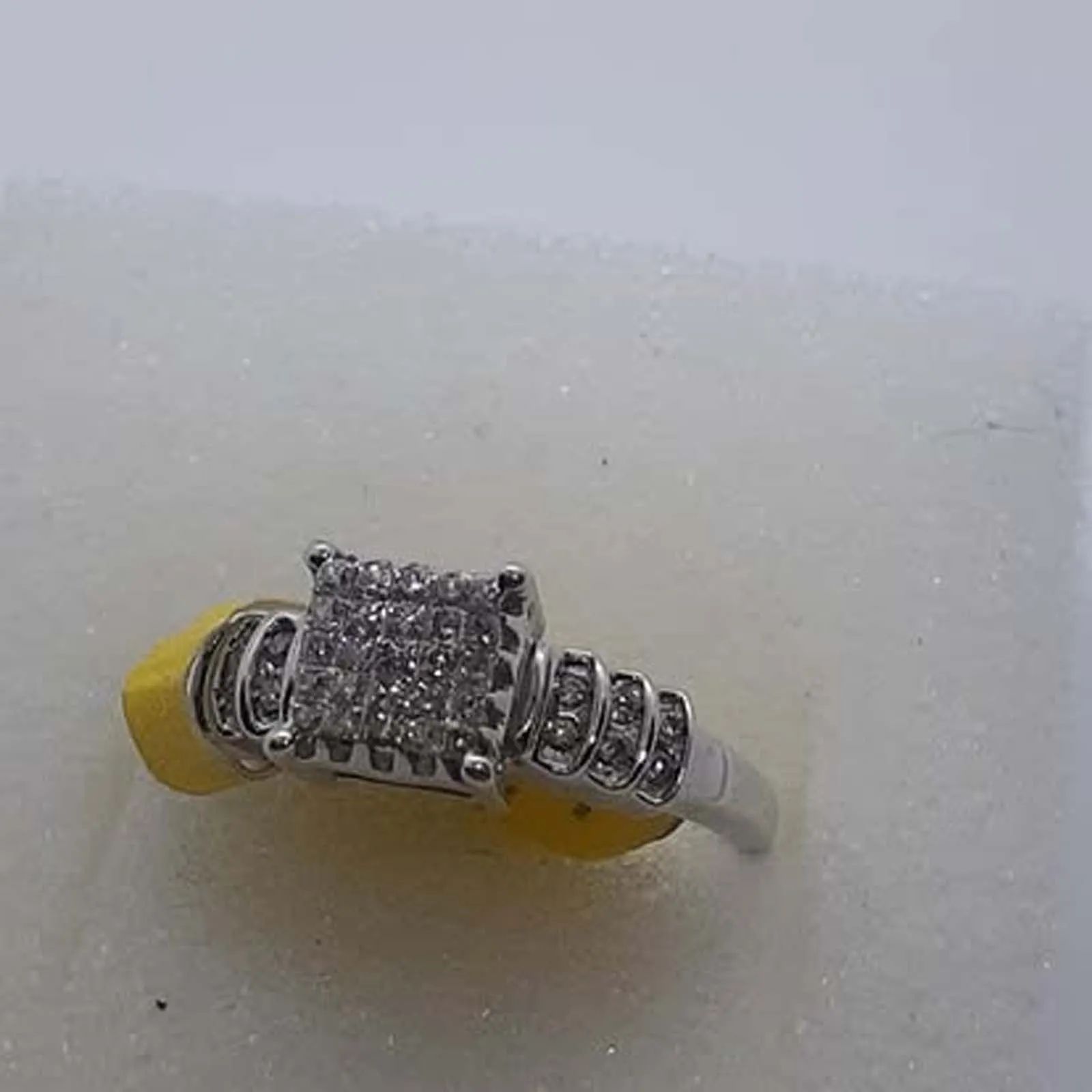 A silver ring with diamonds is sitting on a yellow cushion.