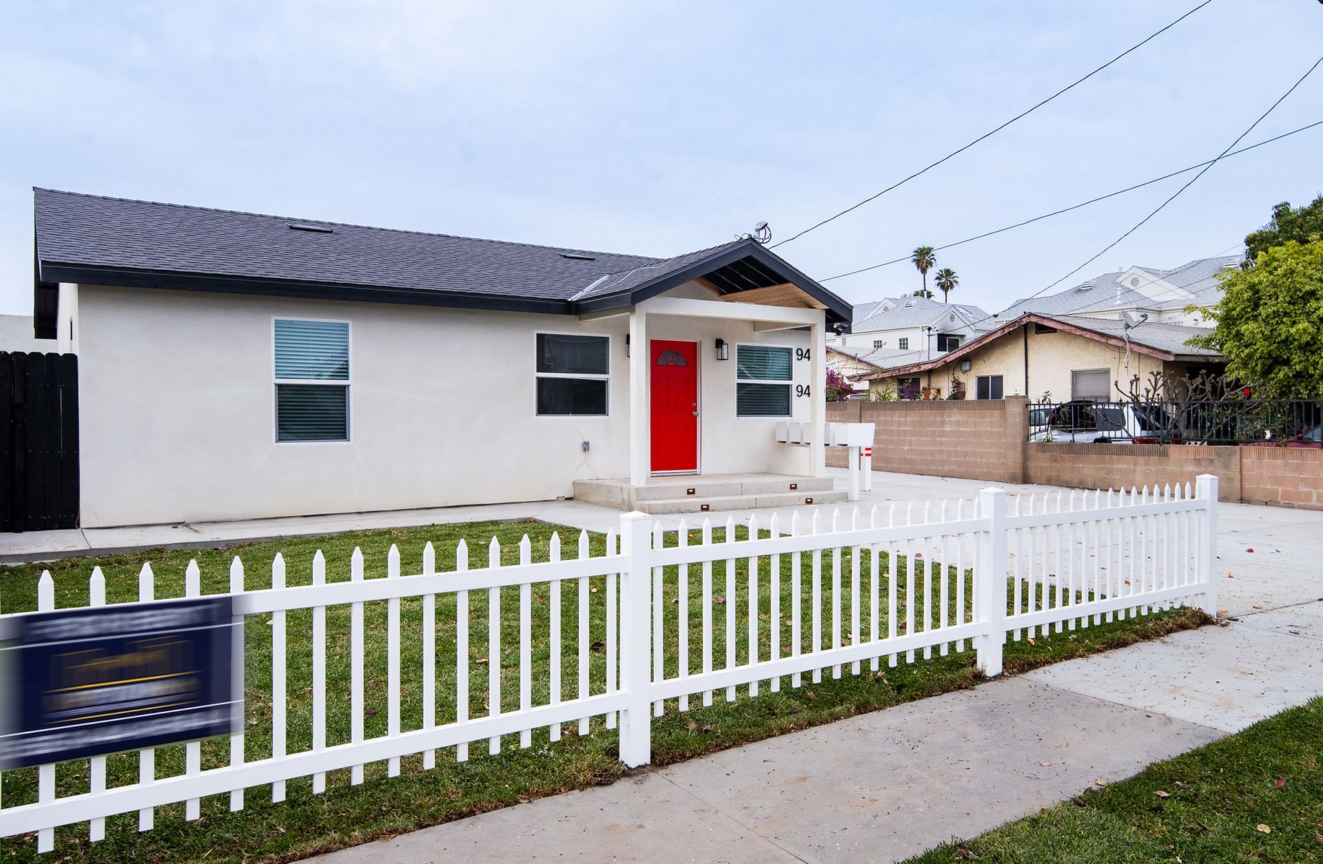 Small white house with a red front door, white picket fence, and a sidewalk in front.