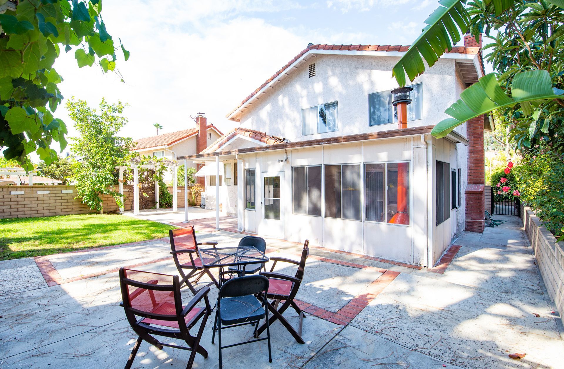 Patio with black chairs and tables outside a white two-story house with screened porch and garden greenery