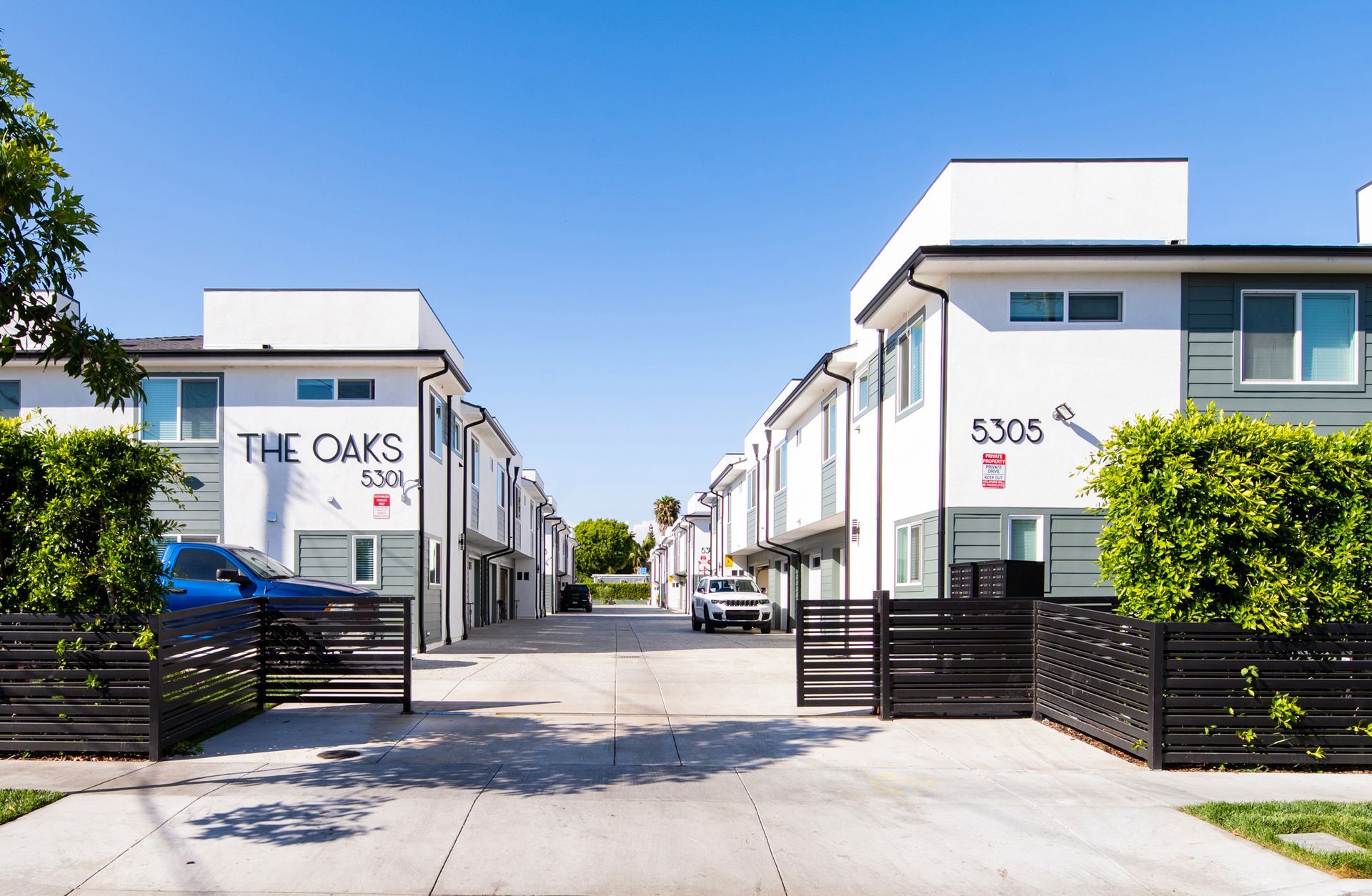 Modern apartment complex entrance with white buildings, black gates, and blue sky