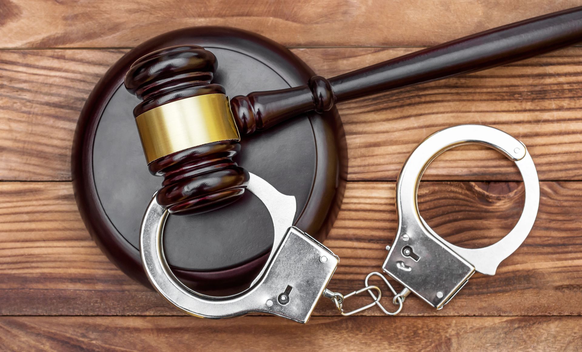 Judge’s gavel beside handcuffs on a wooden surface, symbolizing law enforcement and arrest