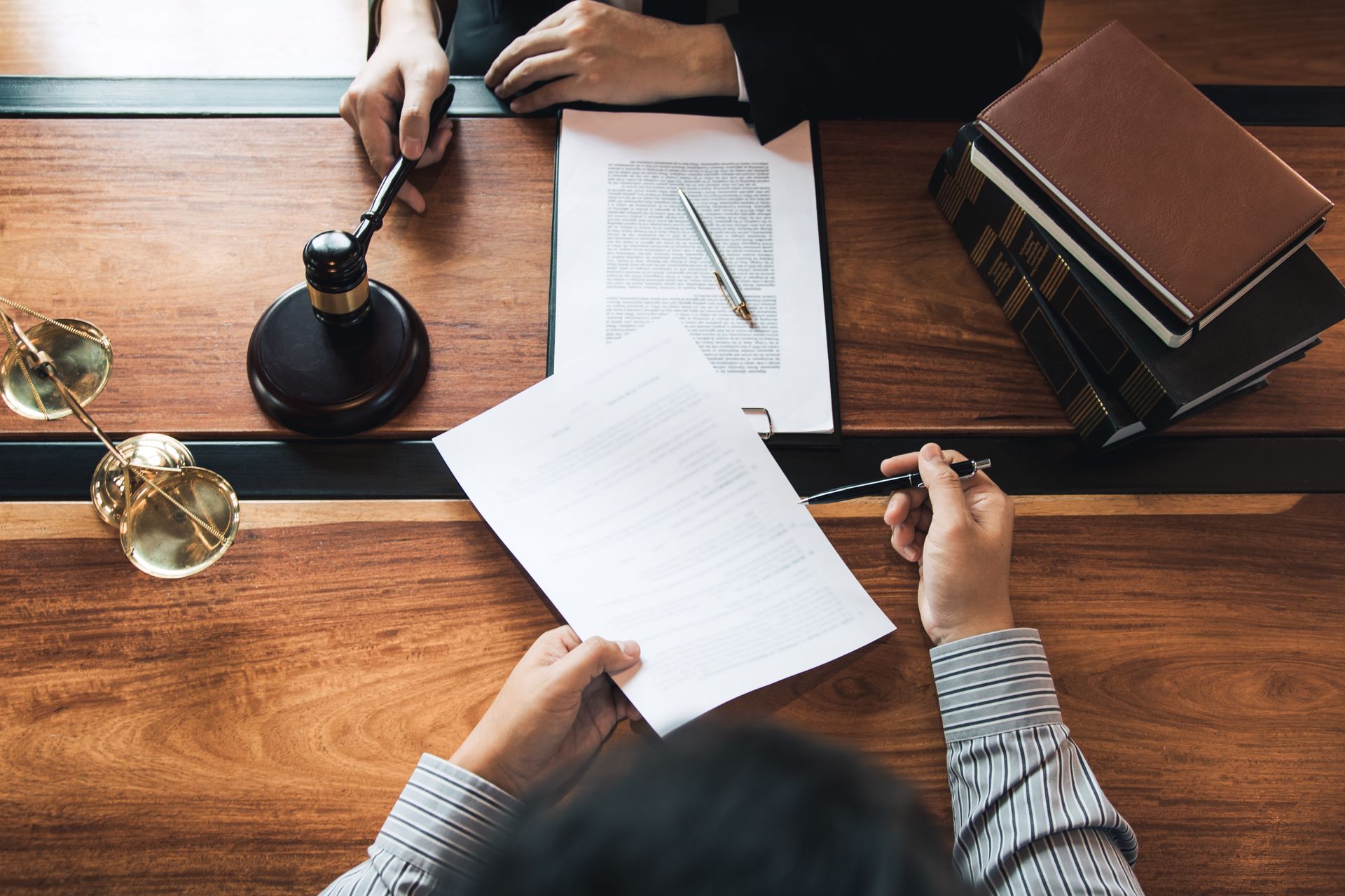 Hands signing a document at a wooden desk with a gavel and books nearby