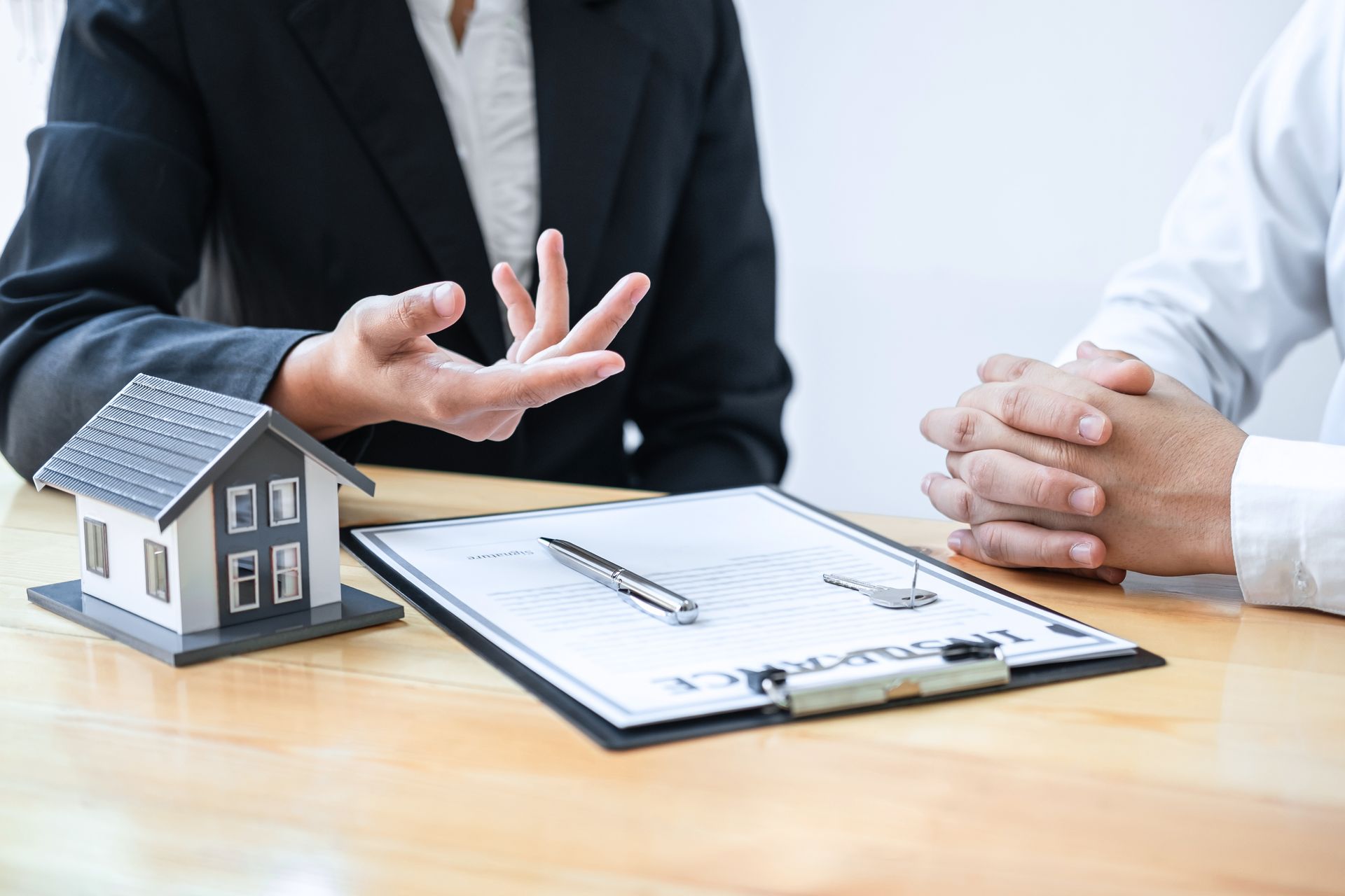 Real estate agent discussing a property sale with client beside a house model and clipboard