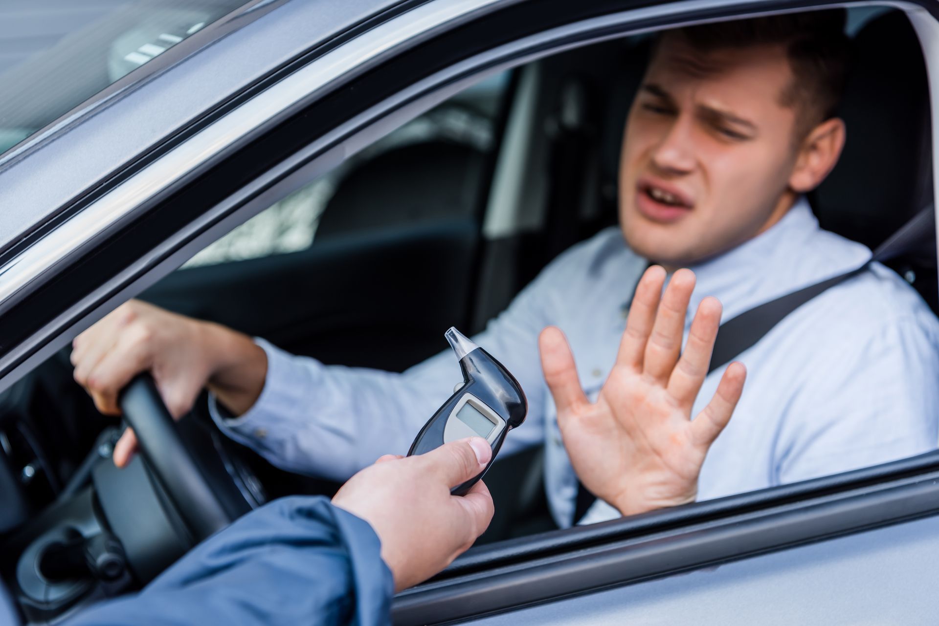 Traffic stop: driver raises hands while officer holds out a breathalyzer beside the car window.