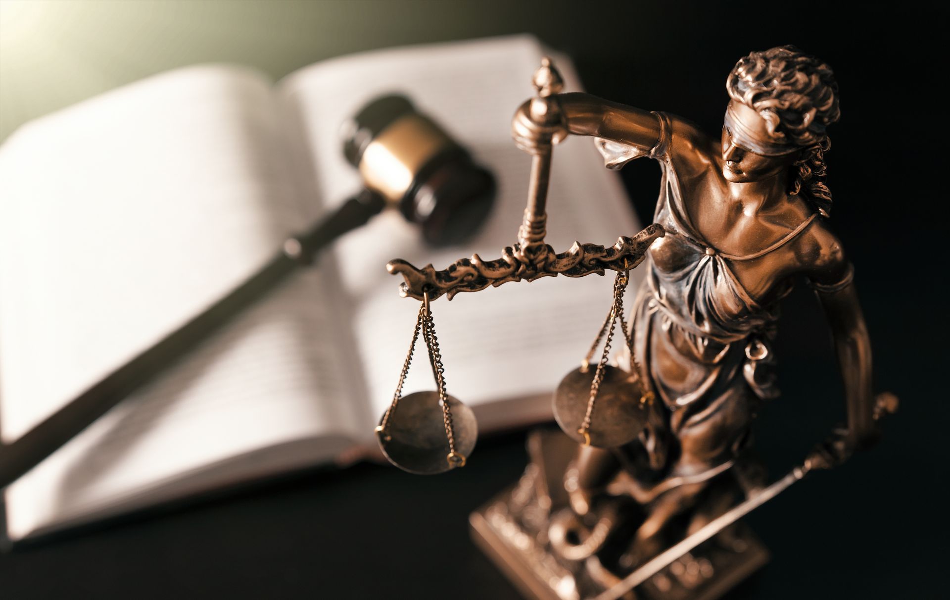 Bronze Lady Justice figurine with scales and gavel in front of an open law book
