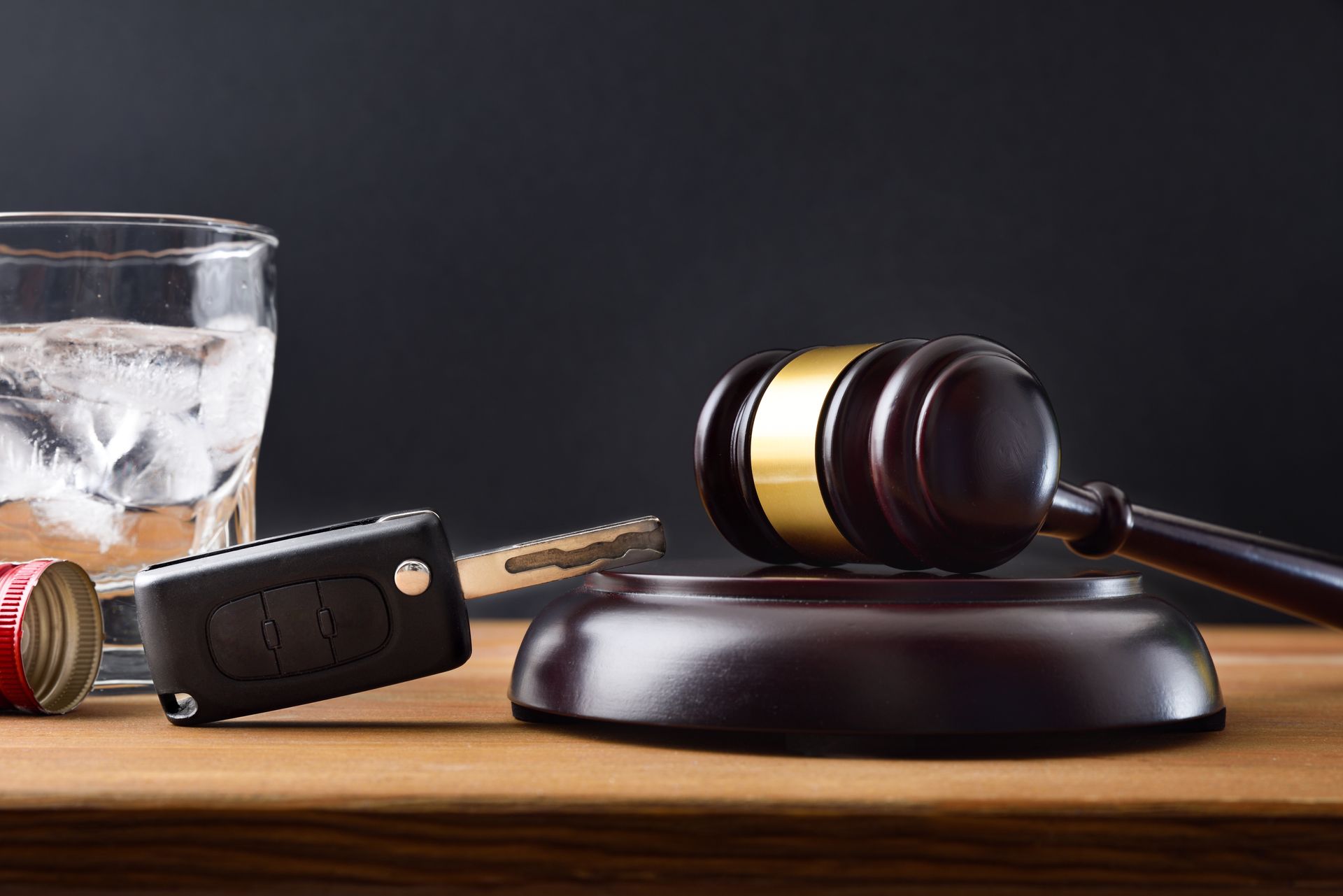 Gavel and judge’s block beside car key, whiskey glass, and handgun on a wooden table