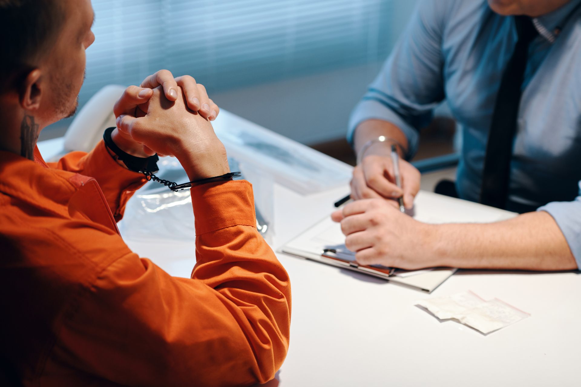 Two people in discussion across a desk, one in an orange shirt and one taking notes on a clipboard