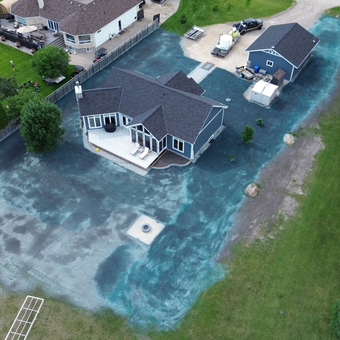Aerial view of a dark-roofed house and a detached garage on a newly seeded lawn; construction vehicles nearby.