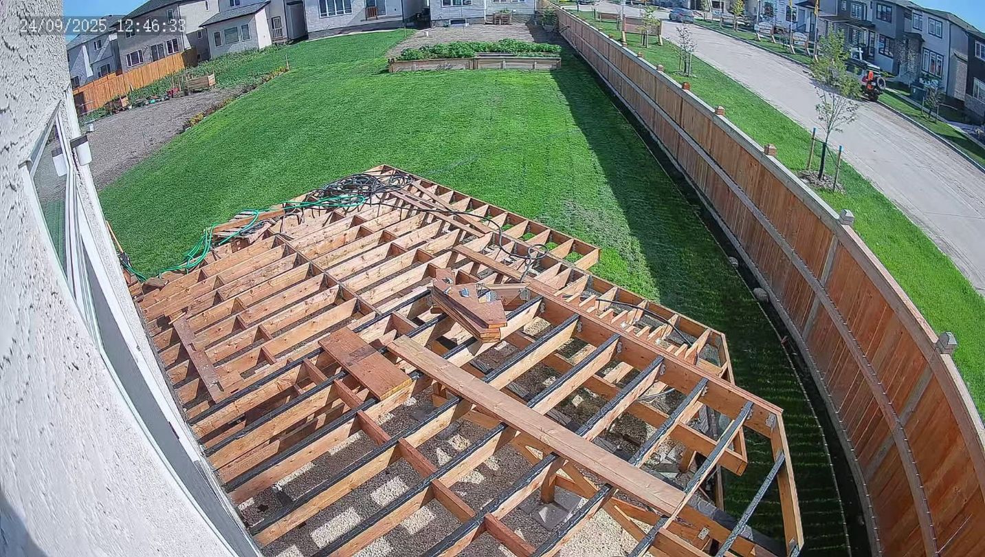 Unfinished deck frame in backyard, green grass, wood fence, residential area, sunny day.