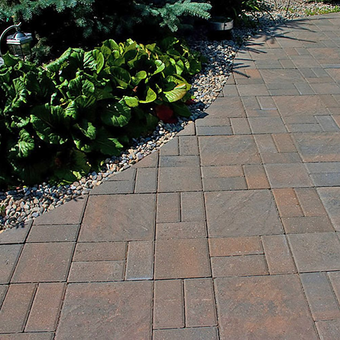 Brick pathway beside a garden bed with lush green plants and small gravel.