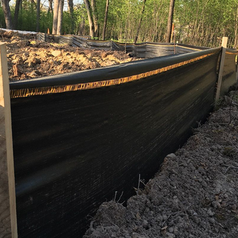 Black silt fence in a construction site, held up by wooden posts.