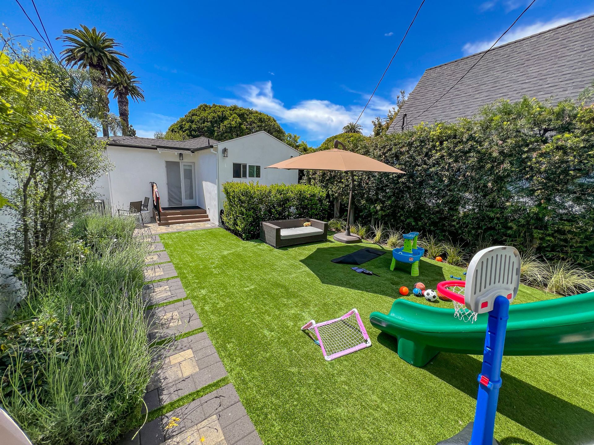 Sunny backyard with lawn, patio umbrella, lounge chairs, and children's water play toys