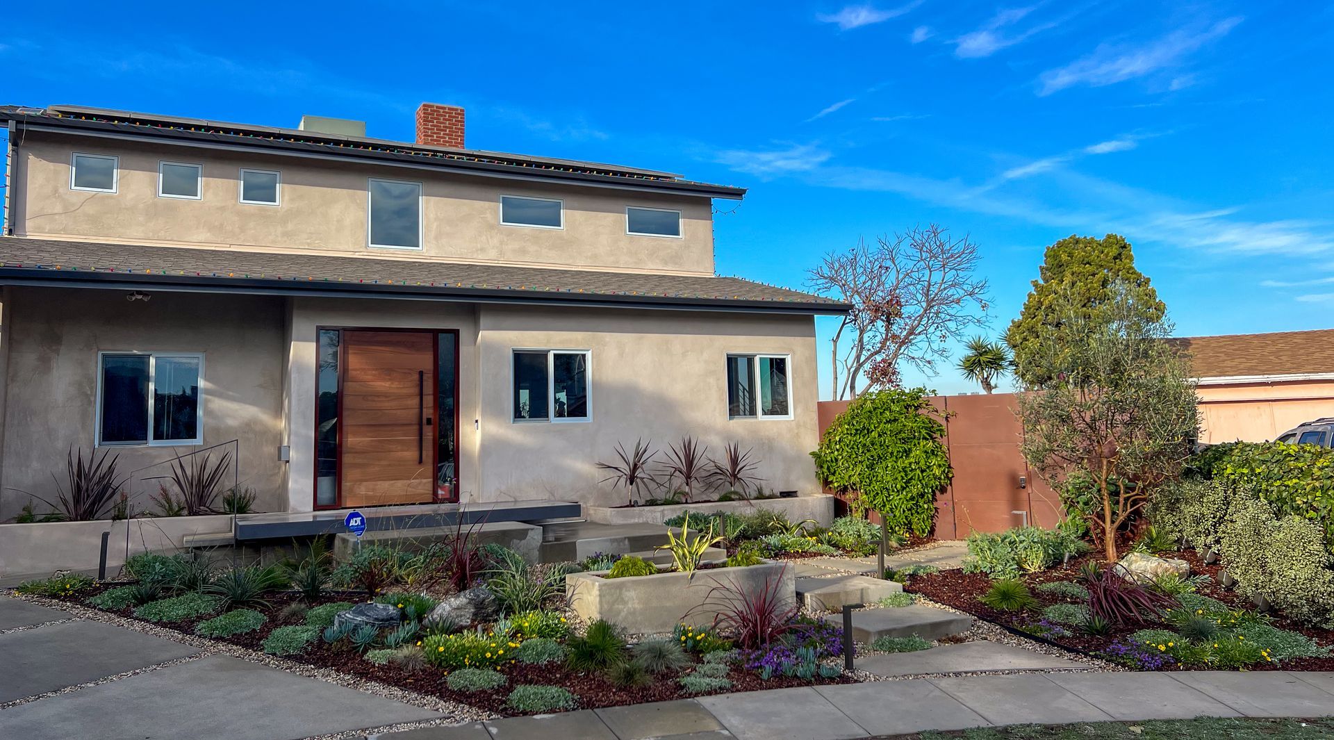 Front view of a tan stucco house with a landscaped front yard and bright blue sky