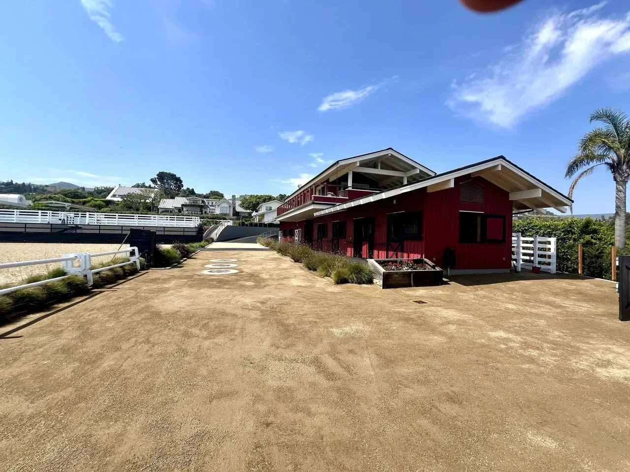 Red wooden building with white trim beside a dry dirt lot under a blue sky