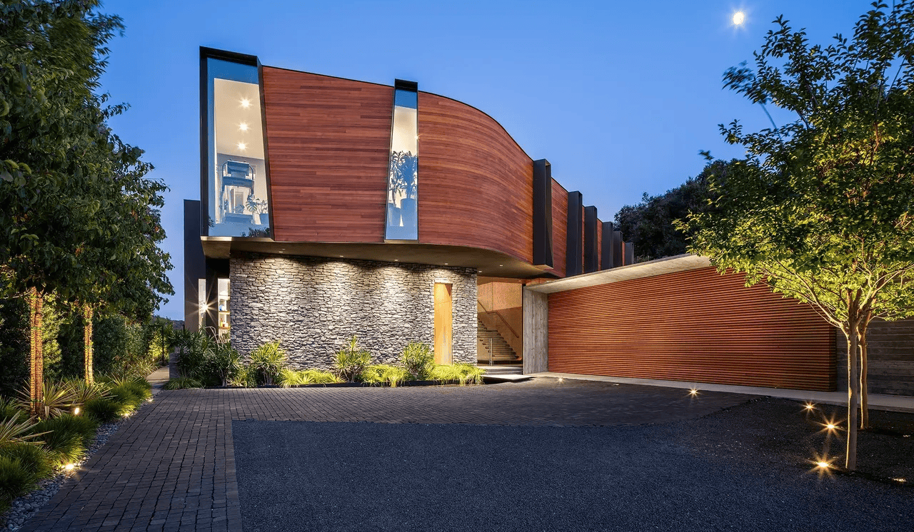 Modern curved brick house with stone entry wall and landscaped driveway at dusk