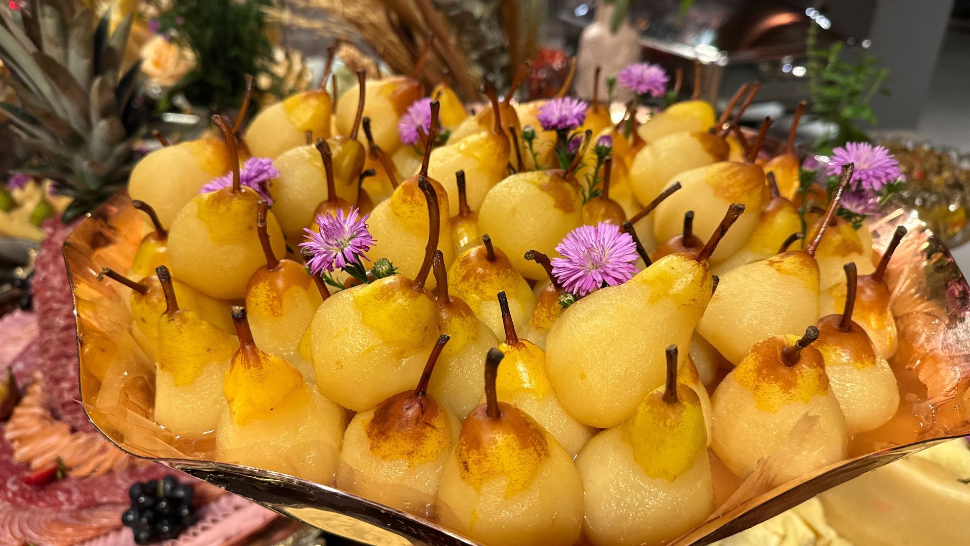 Um prato de peras com flores roxas em cima de uma mesa.