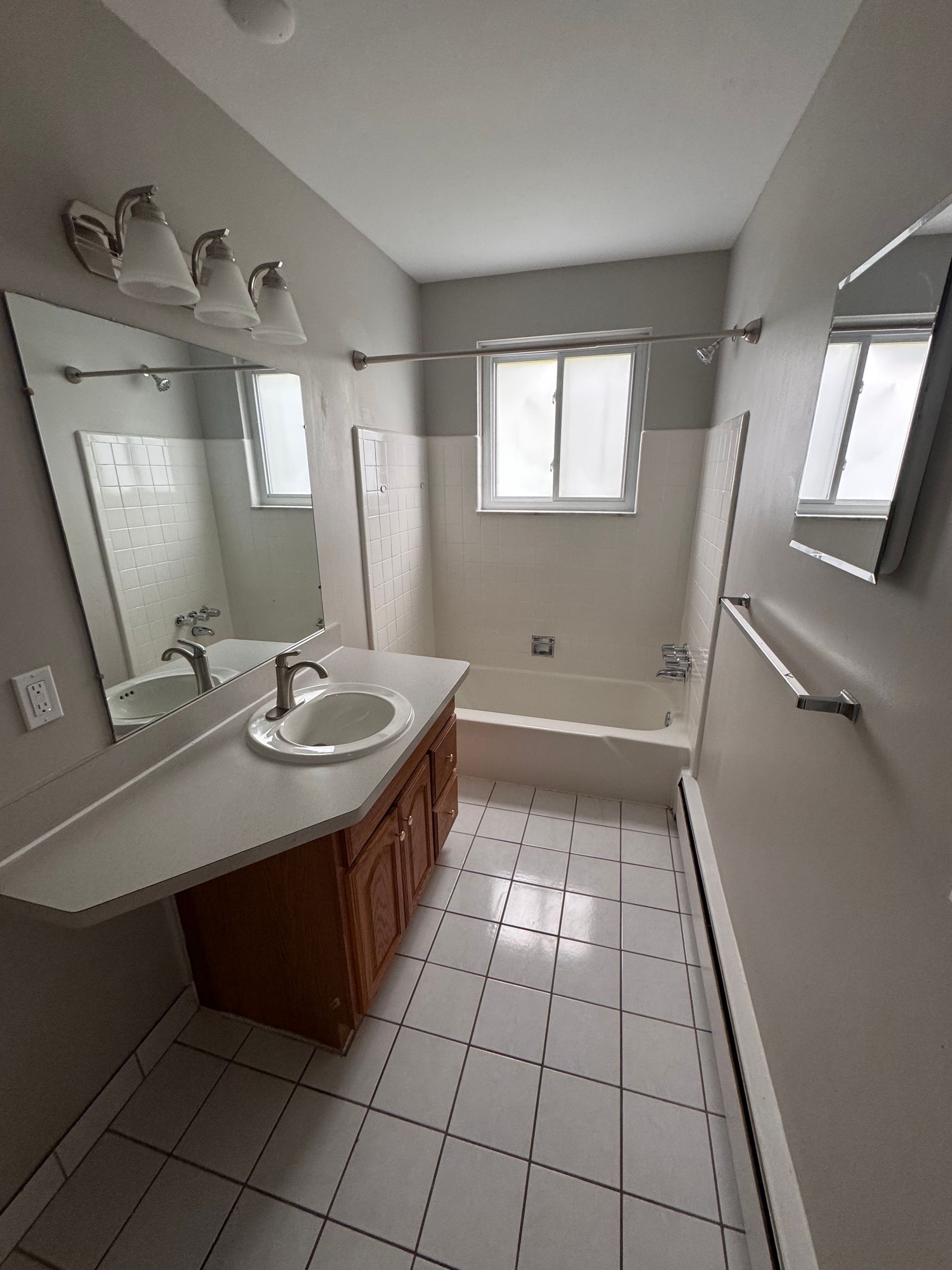 A bathroom with a sink , tub , mirror and window