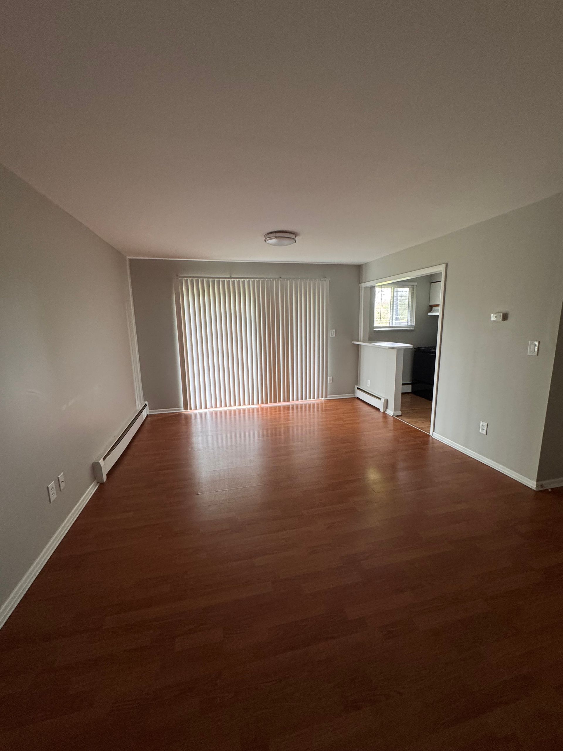 An empty living room with hardwood floors and a sliding glass door.