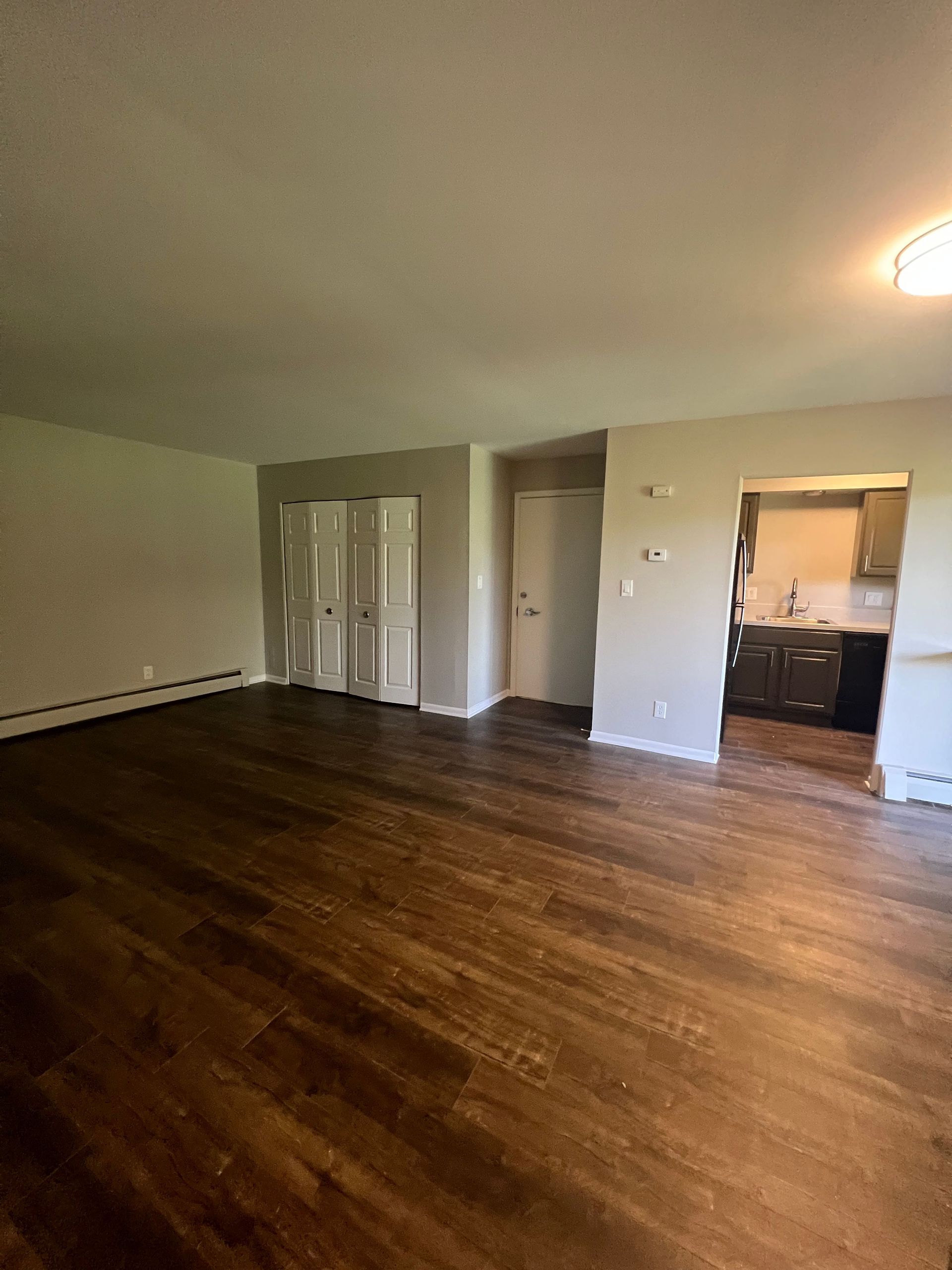 A living room with hardwood floors and a kitchen in the background.