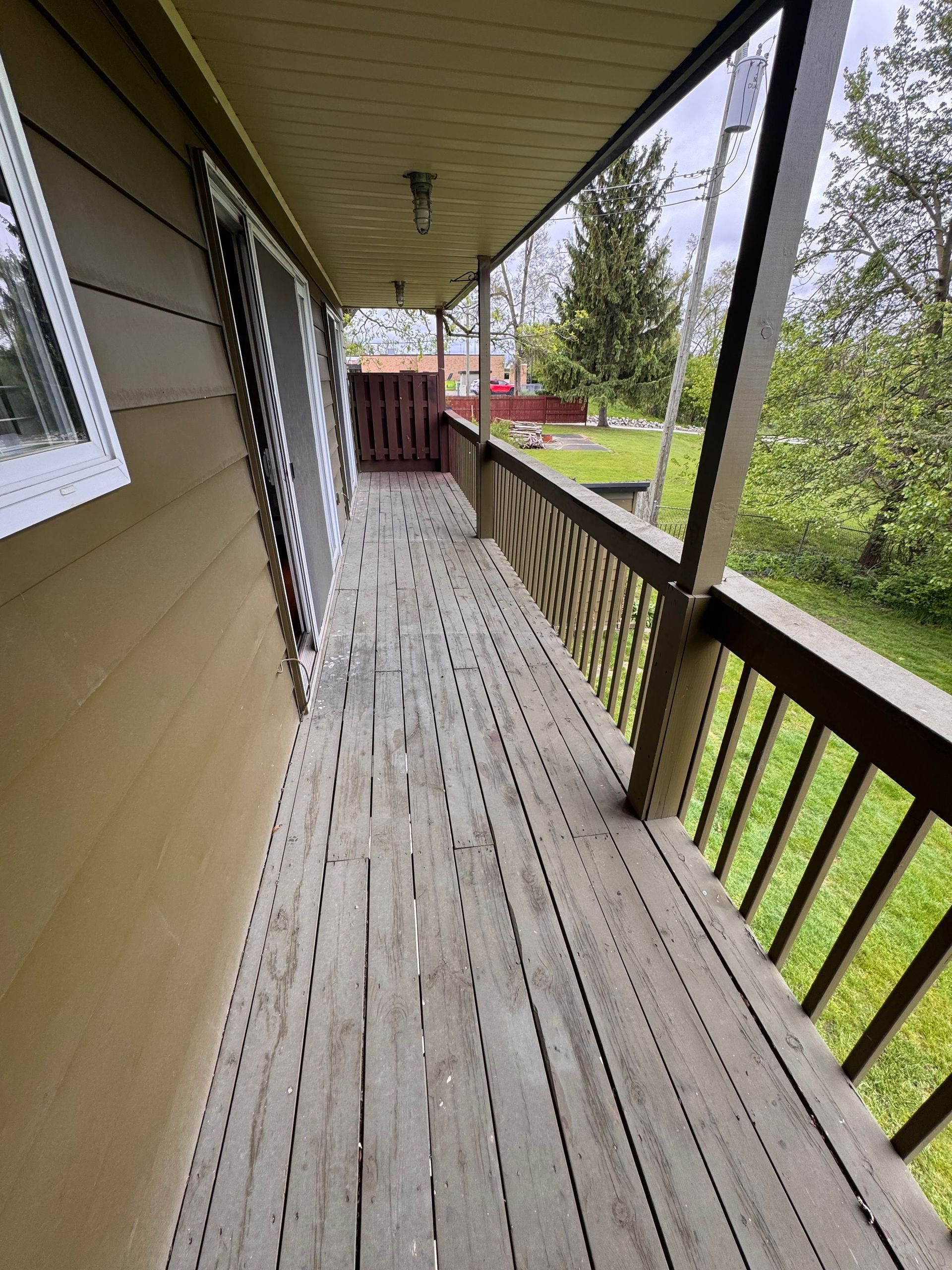 A long wooden porch with a railing and a window on the side of a house.