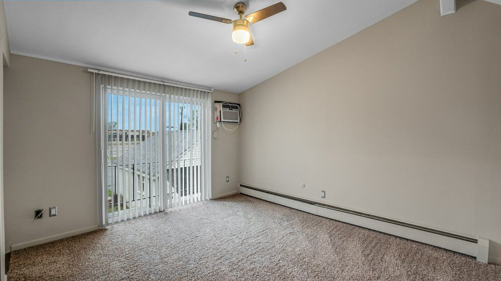 An empty living room with a ceiling fan and sliding glass doors.