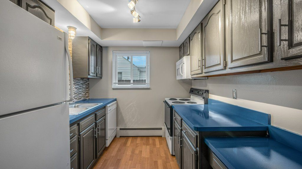 A kitchen with blue counter tops , white cabinets , a refrigerator , and a window.