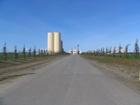 a road leading to a factory with silos in the background