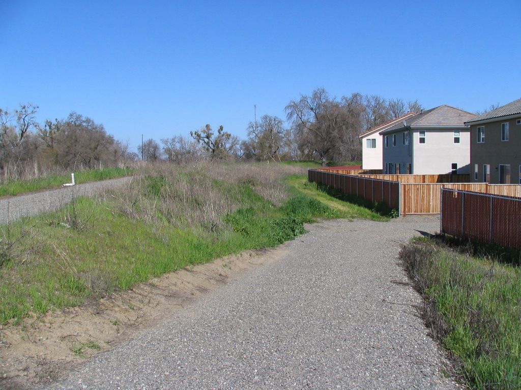 a gravel road leading to a house with a wooden fence