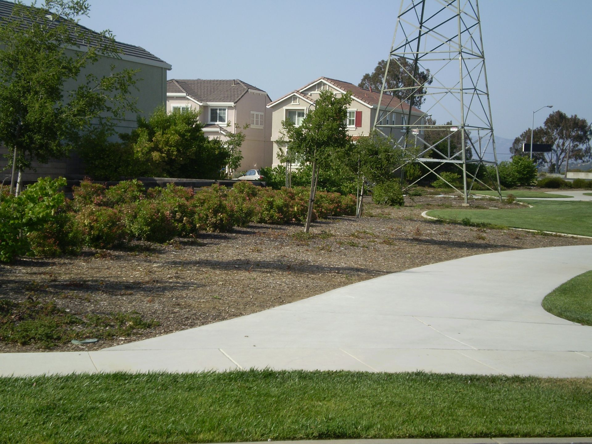 a concrete walkway in a park with a power tower in the background