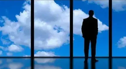 A man standing looking out of a window to a blue sky