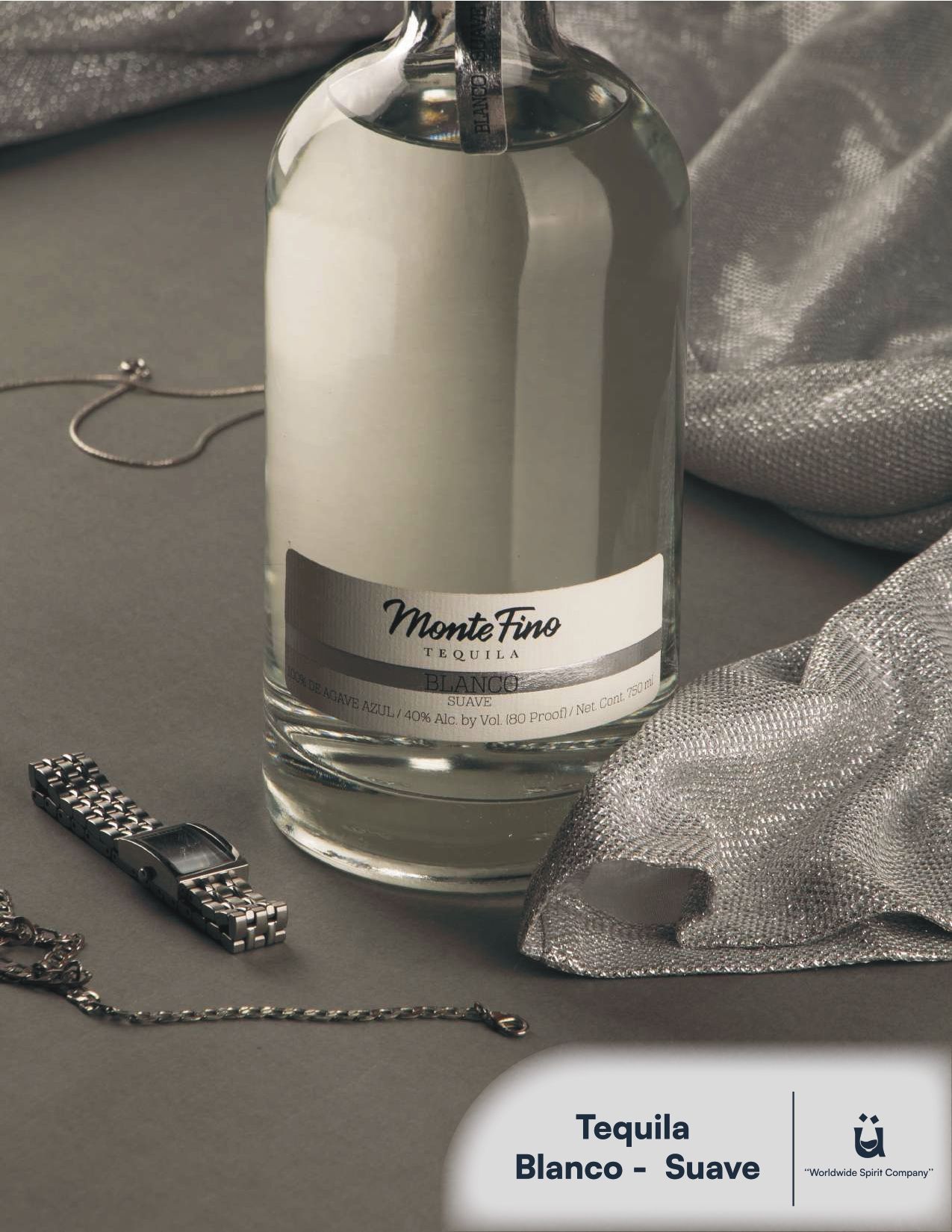 Bottle of Monte Fino tequila with a silver label on a gray surface with silver fabric and jewelry.