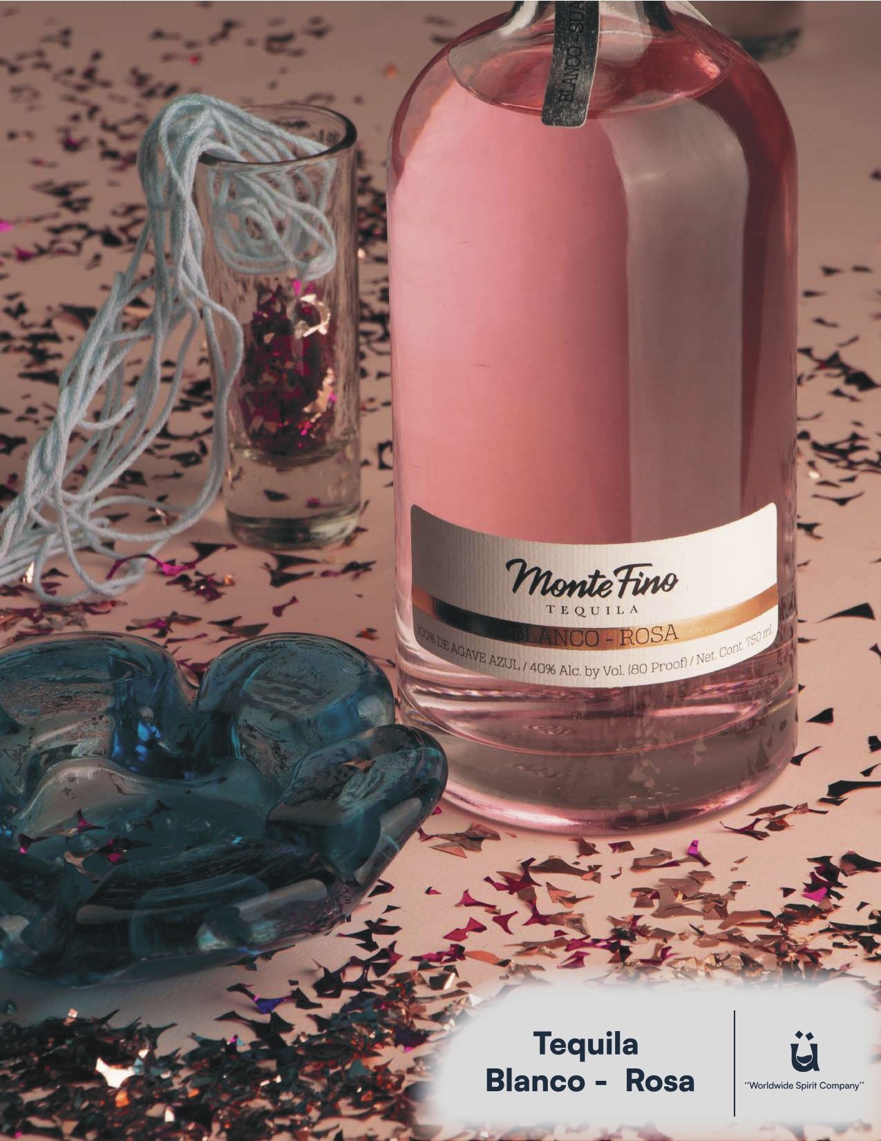 Bottle of pink tequila, shot glass, and blue glass dish on a surface scattered with confetti.