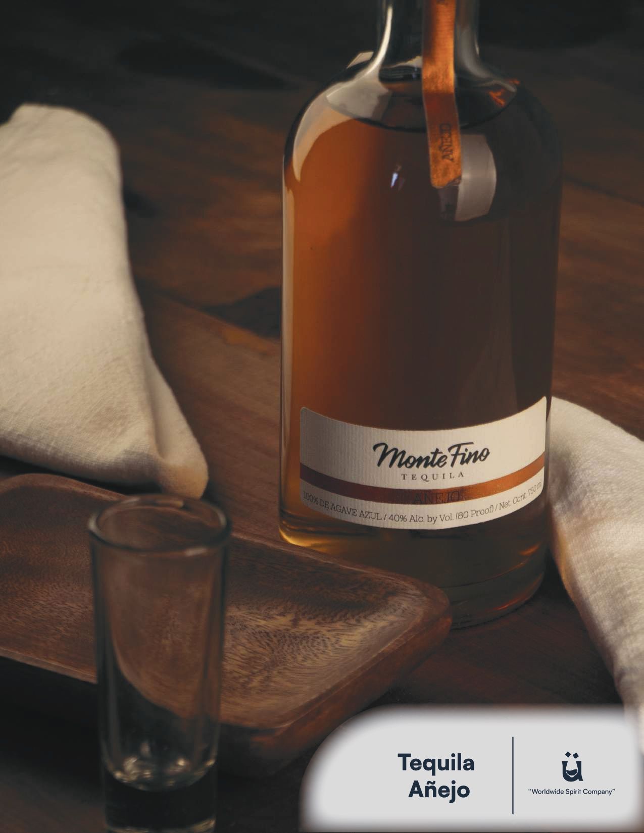 Bottle of Monte Fino Añejo tequila with a shot glass and wooden tray on a wooden surface.