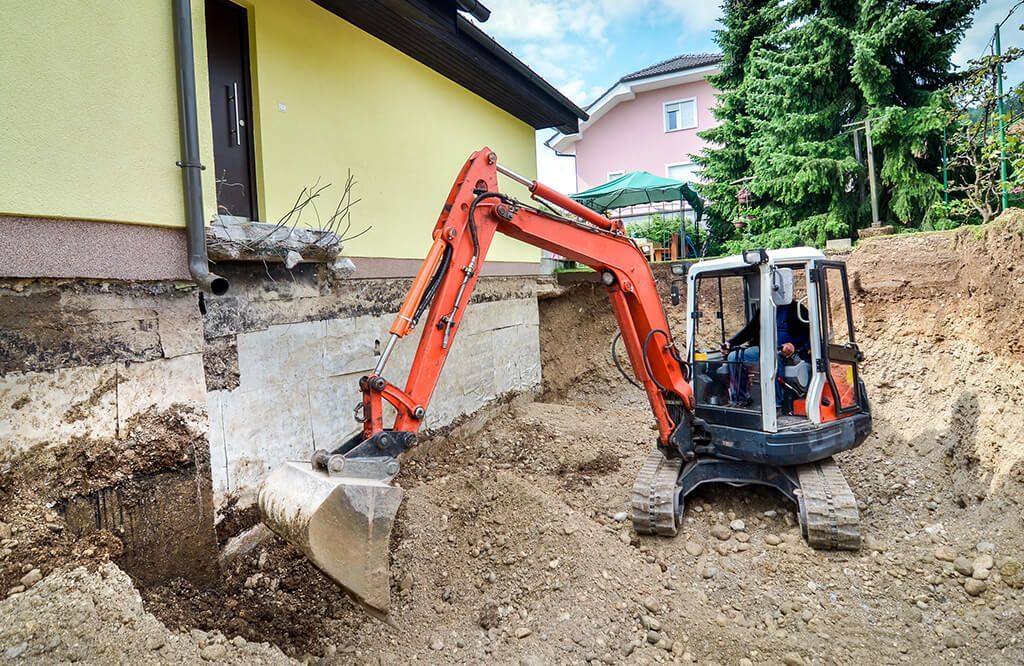 An excavator is digging a hole in front of a house.