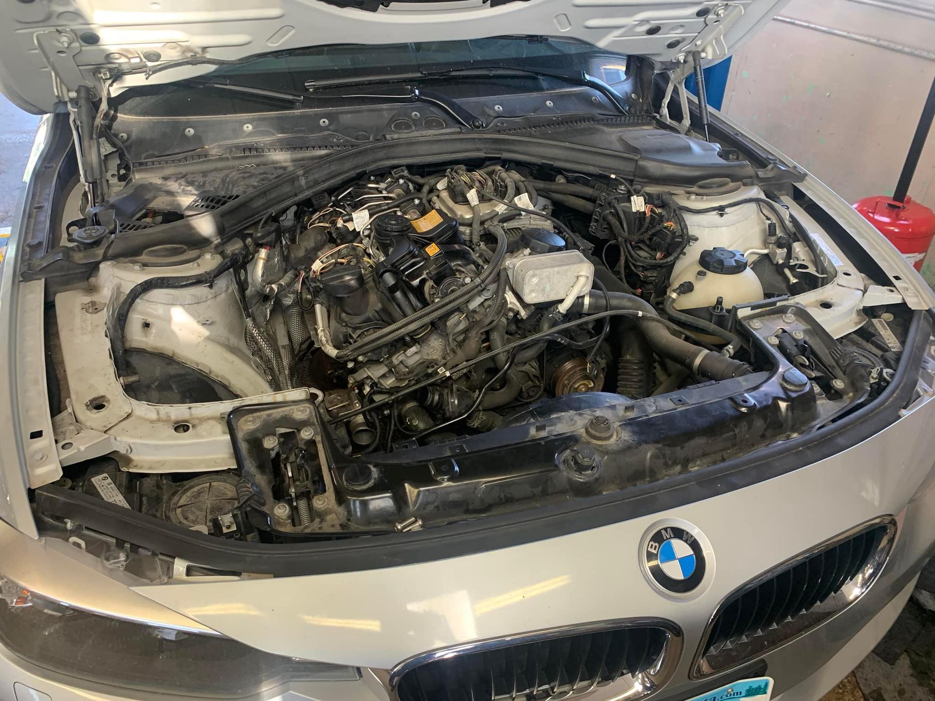 Open hood of a silver BMW car, revealing the engine compartment, likely for servicing.