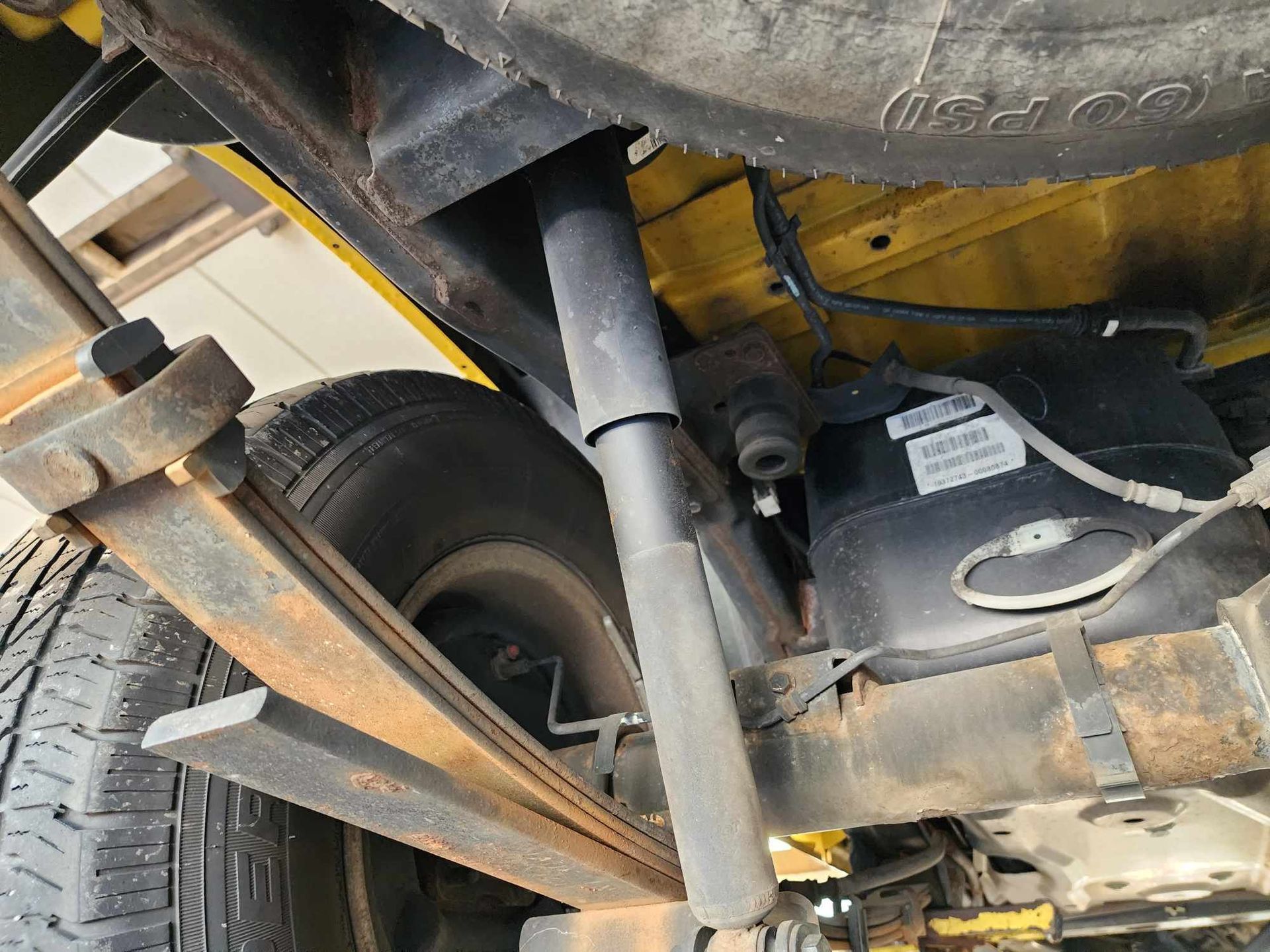 Undercarriage view: Yellow vehicle with rusty leaf spring, shock absorber, and black components.