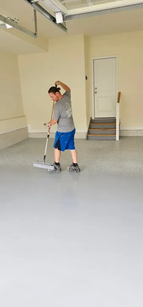 A man is painting a garage floor with a roller.