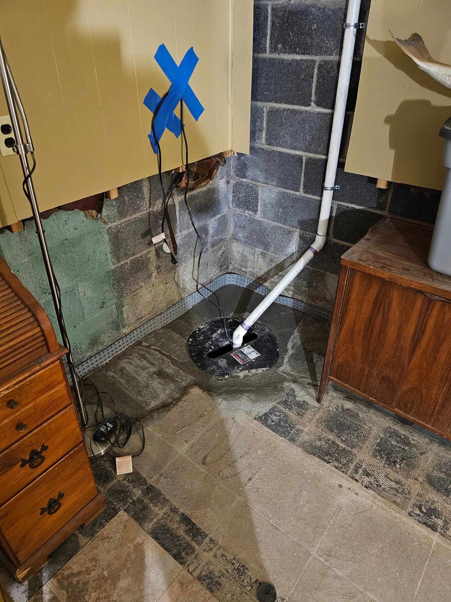 A basement with a drain and a blue tape on the wall.
