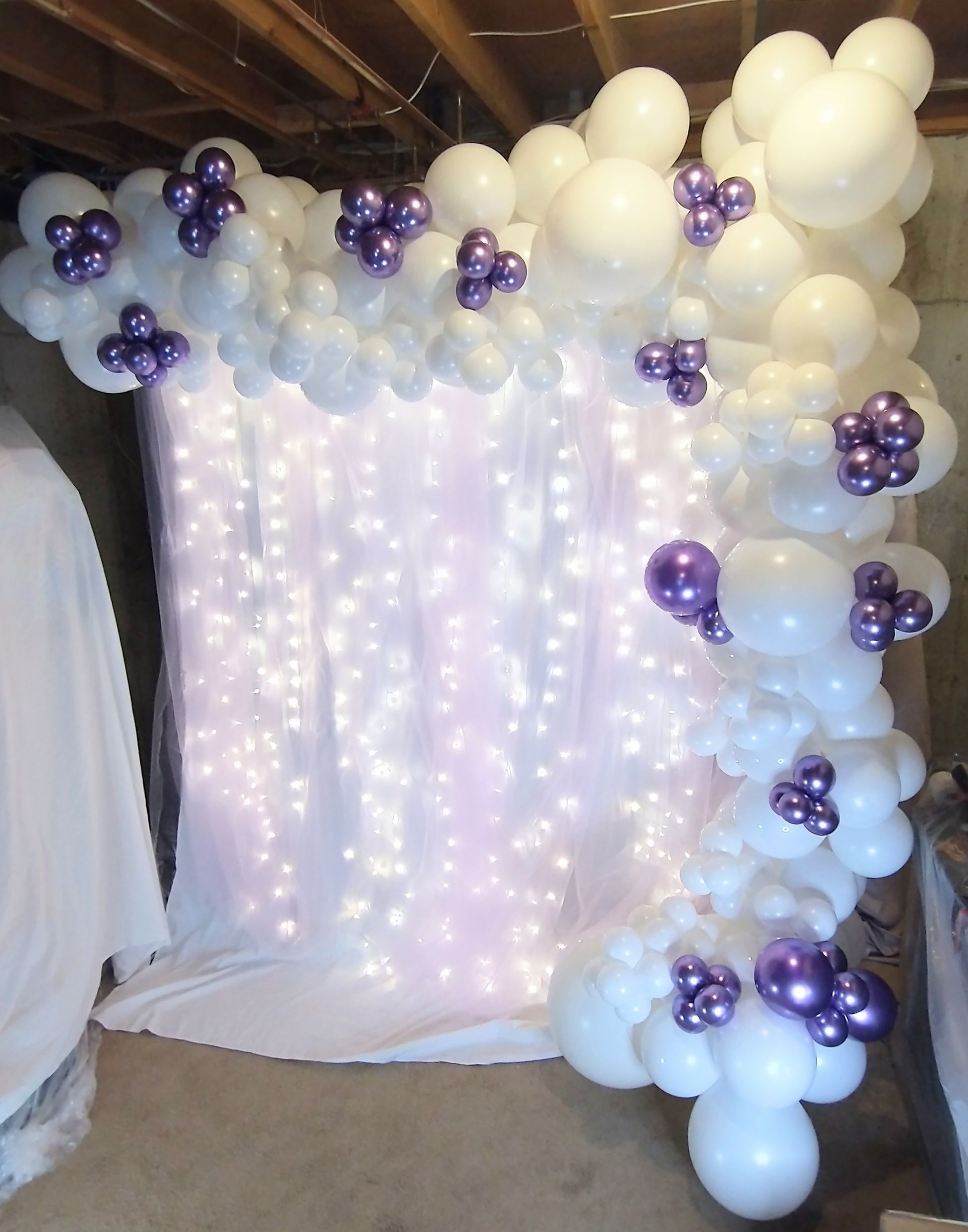 A bunch of white balloons and purple balloons are hanging from a wall.