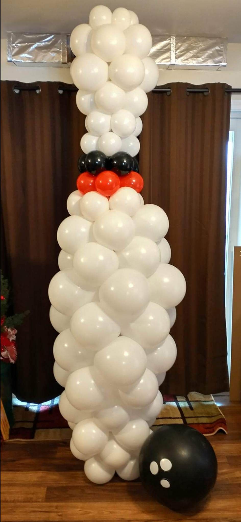 A bowling pin made out of balloons is sitting next to a bowling ball.