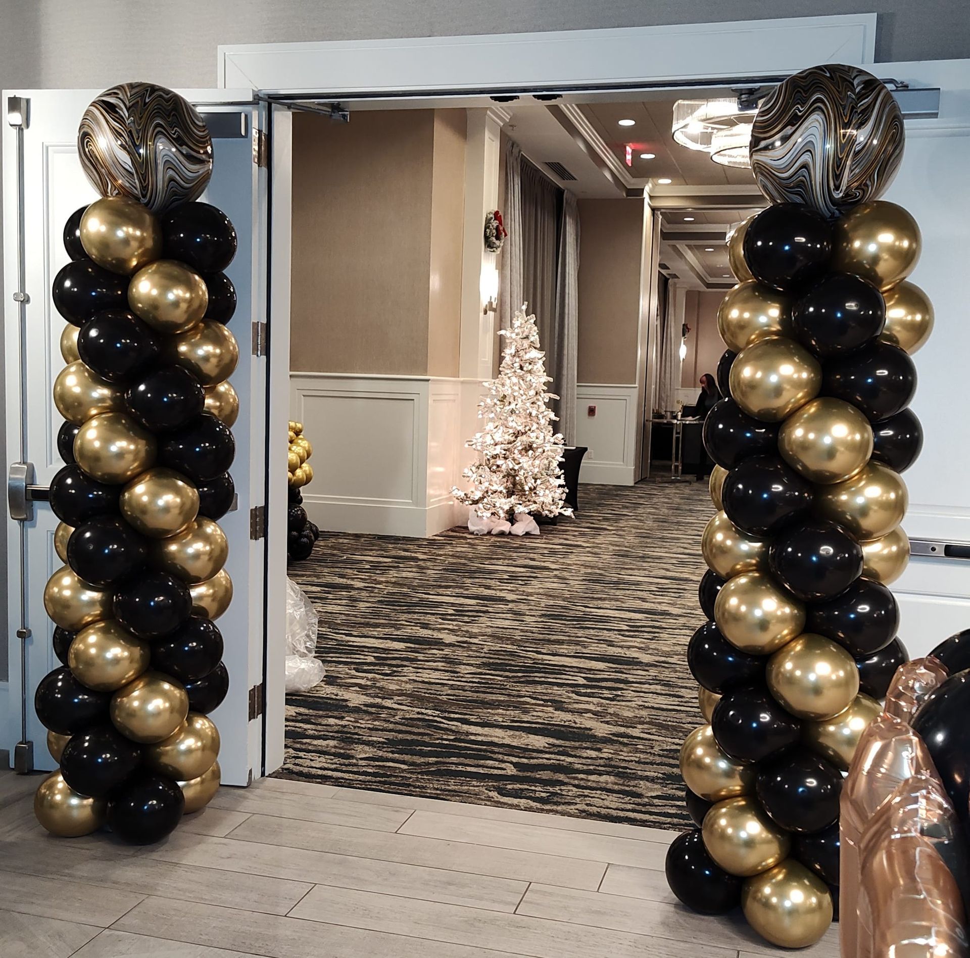 Black and gold balloons are lined up in a hallway