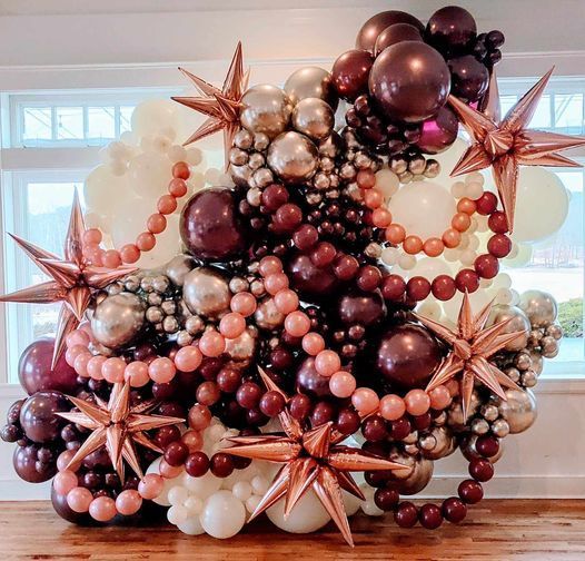 A wall of balloons and beads in a room with a window.