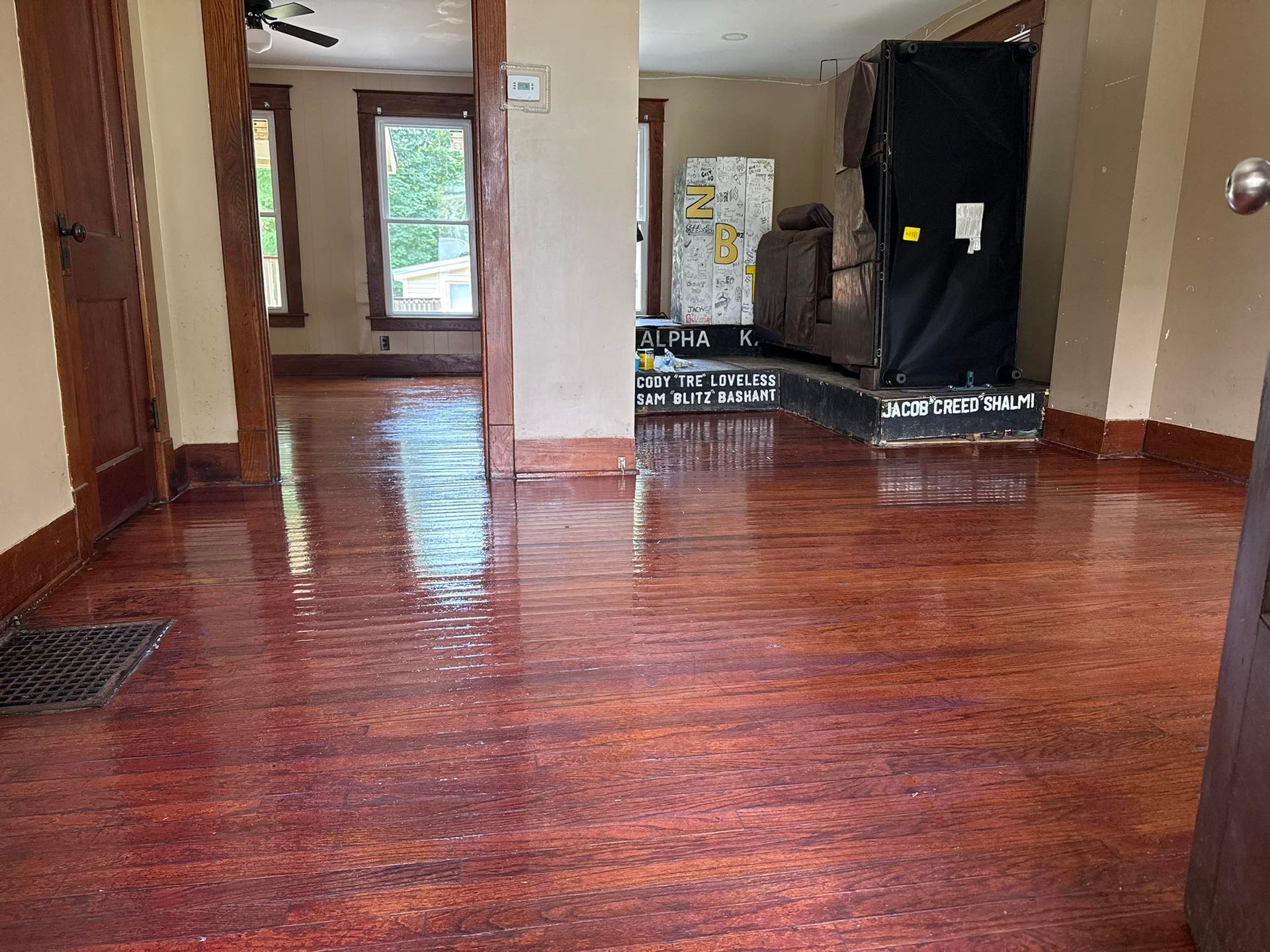 Interior view: Glossy reddish-brown floor, dark wooden trim, doorway to hallway with window, appliance covered in black.