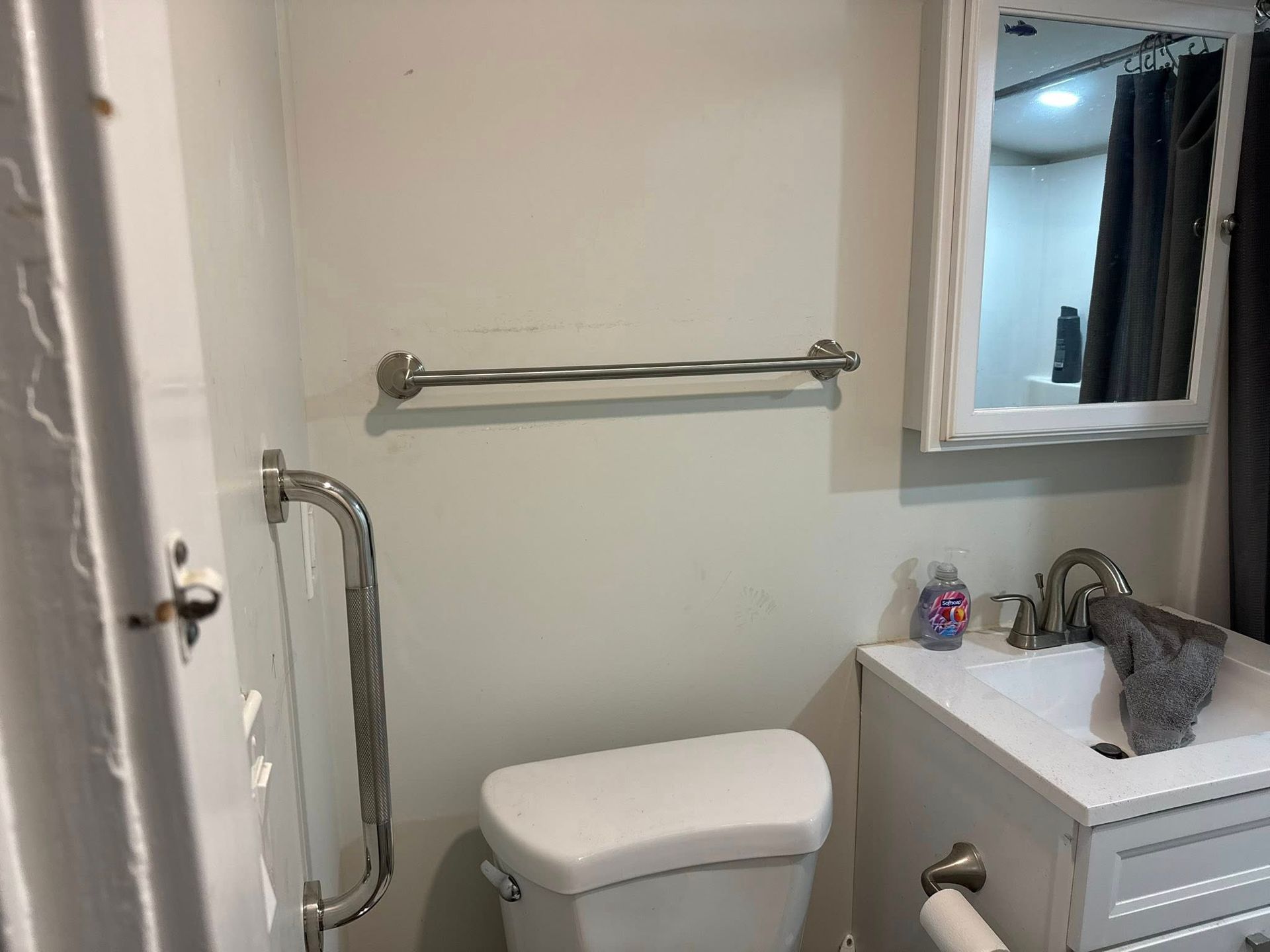Bathroom with toilet, sink, mirror, towel bar, and grab bar on wall.